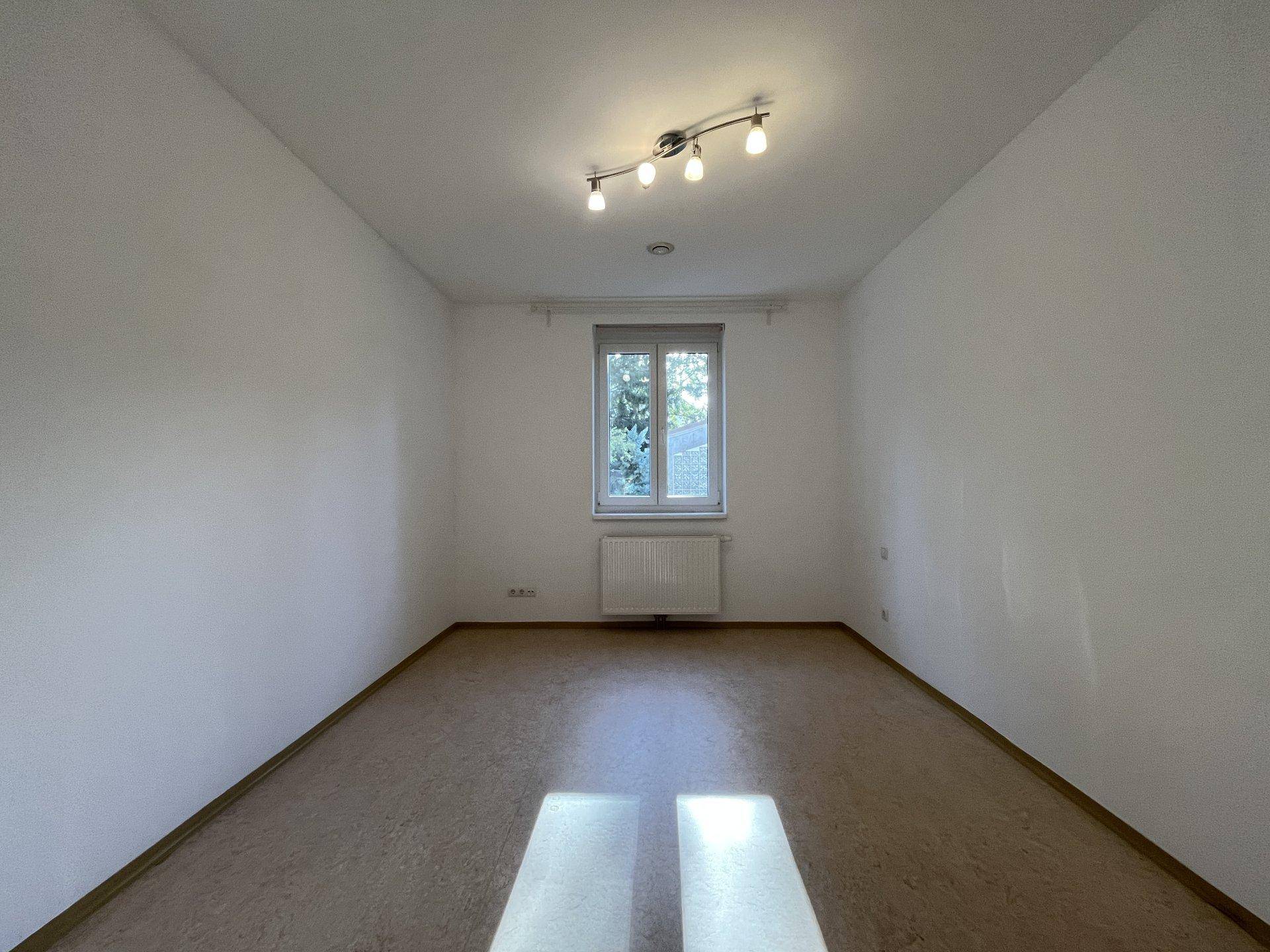 Heller, leerer Raum mit Fenster und Heizkörper, ideal für Schlaf- oder Wohnbereich.