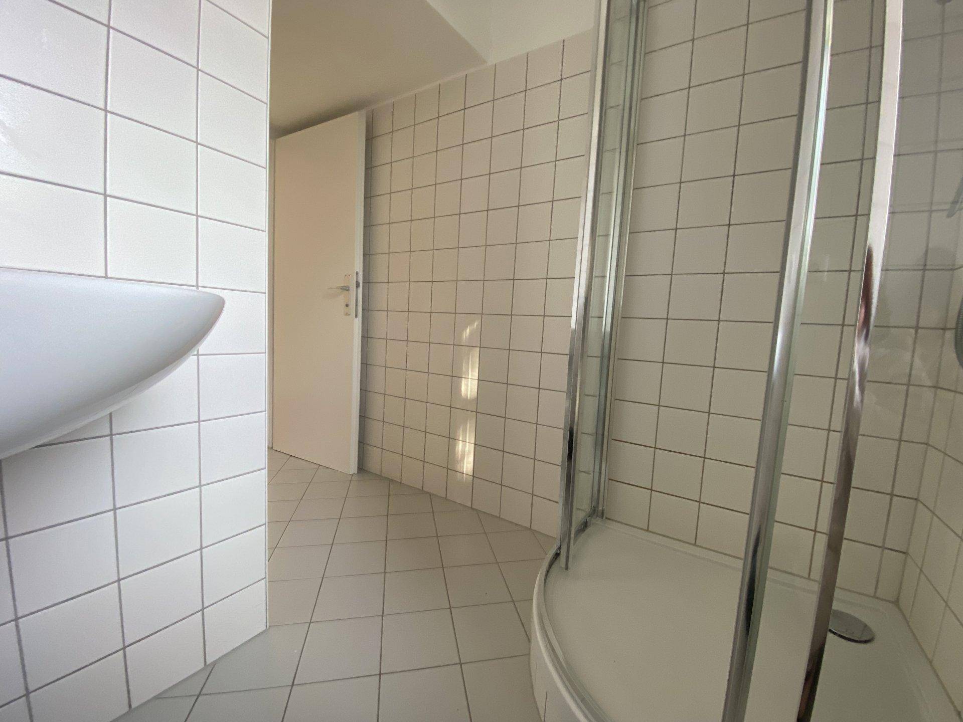 Badezimmer mit weißen Fliesen, einer Duschkabine und einem Waschbecken, das viel Tageslicht erhält.