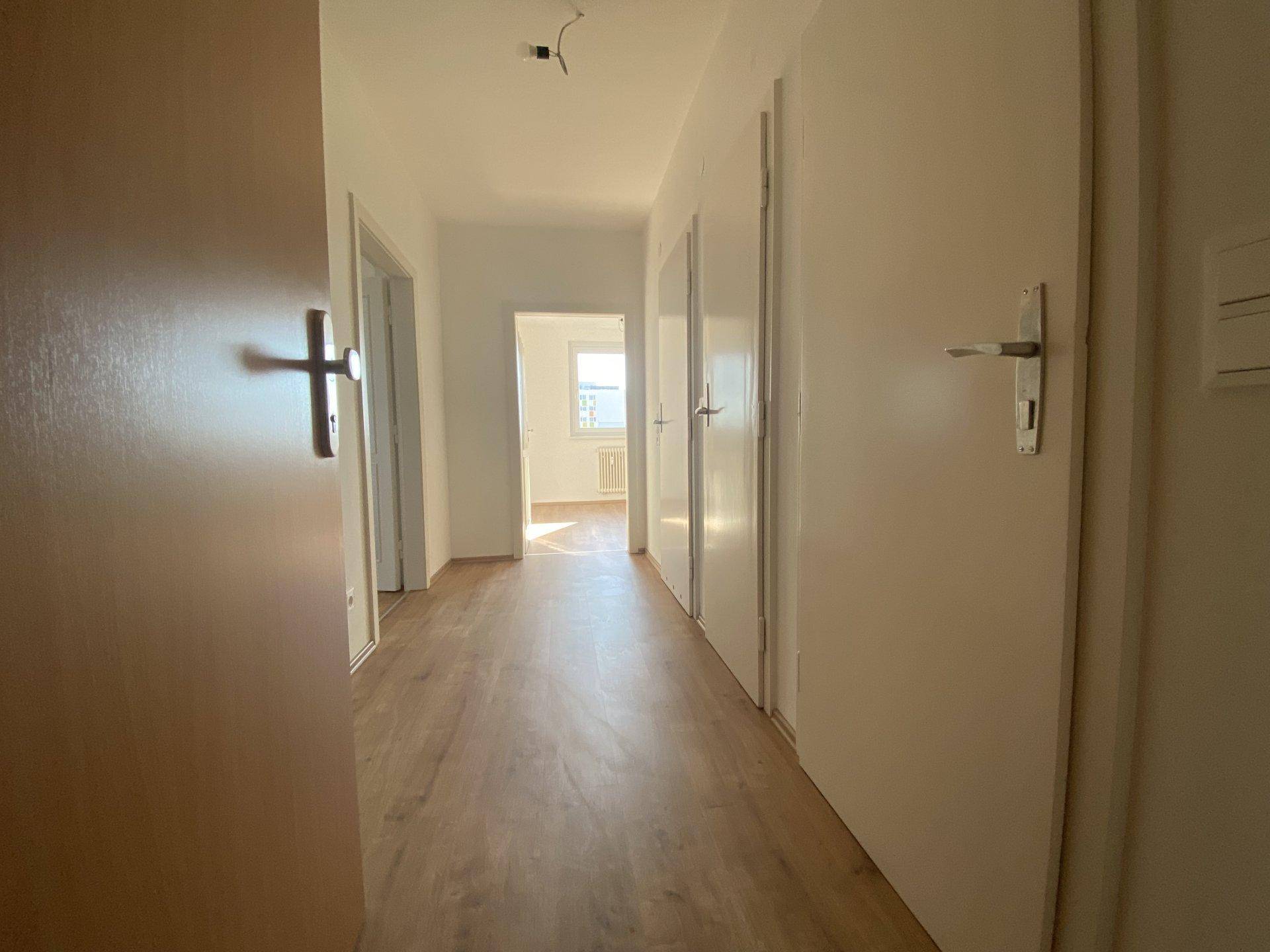 Heller Flur mit Laminatboden und mehreren Türen, der zu weiteren Räumen führt.