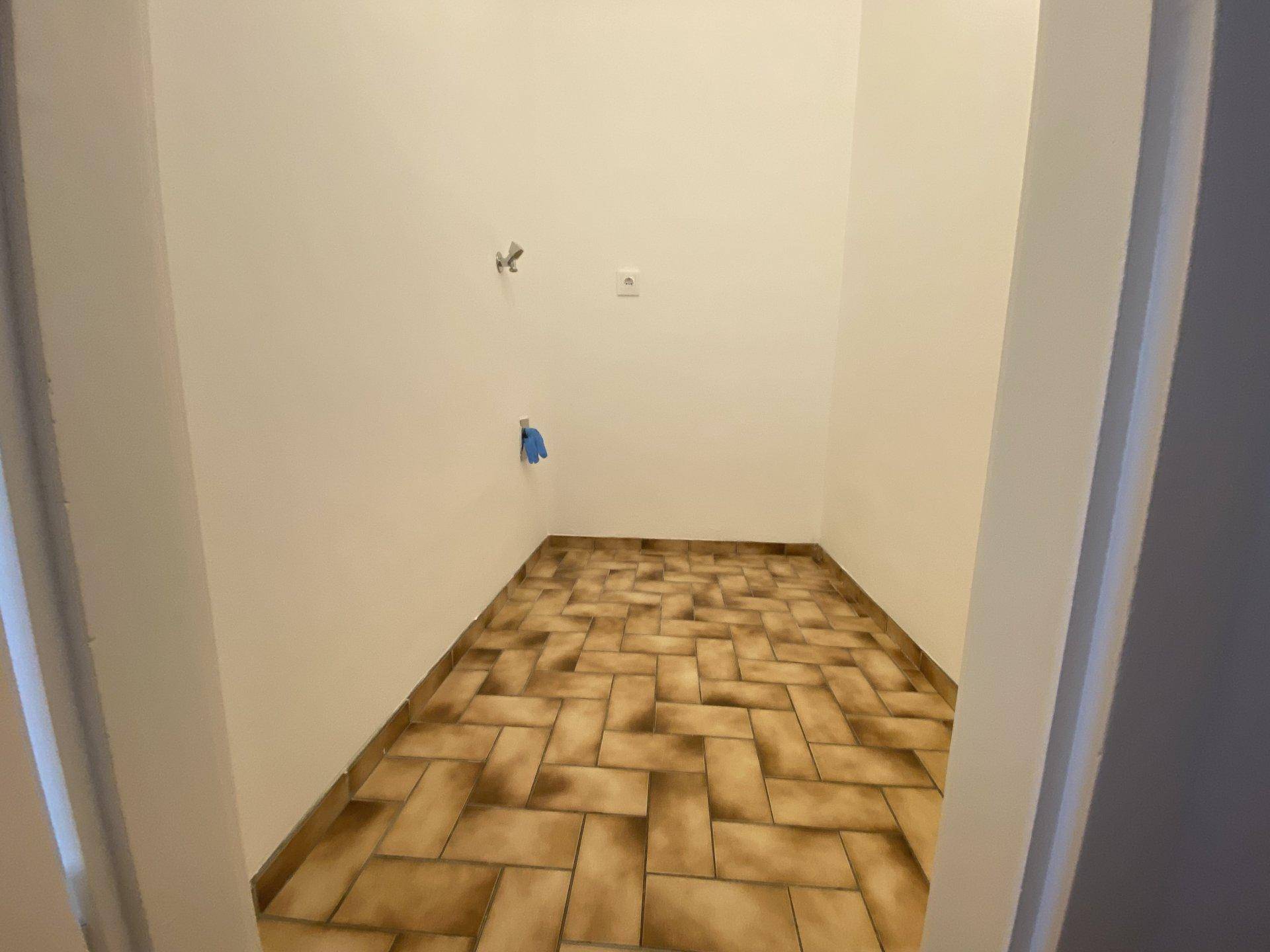 Kleiner Hauswirtschaftsraum mit Fliesenboden und Anschlüssen für eine Waschmaschine.