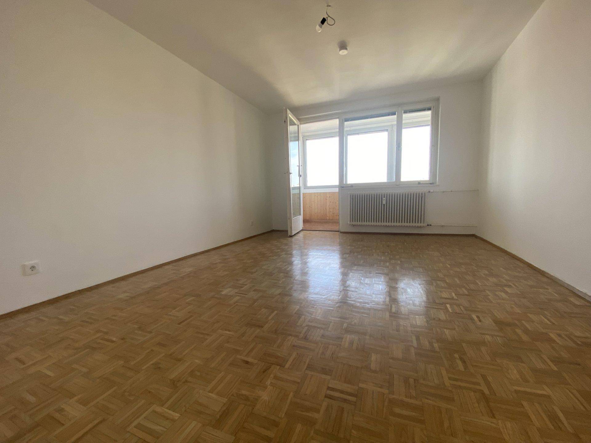 Geräumiges Zimmer mit Parkettboden und Zugang zu einem kleinen Balkon, hell und einladend.