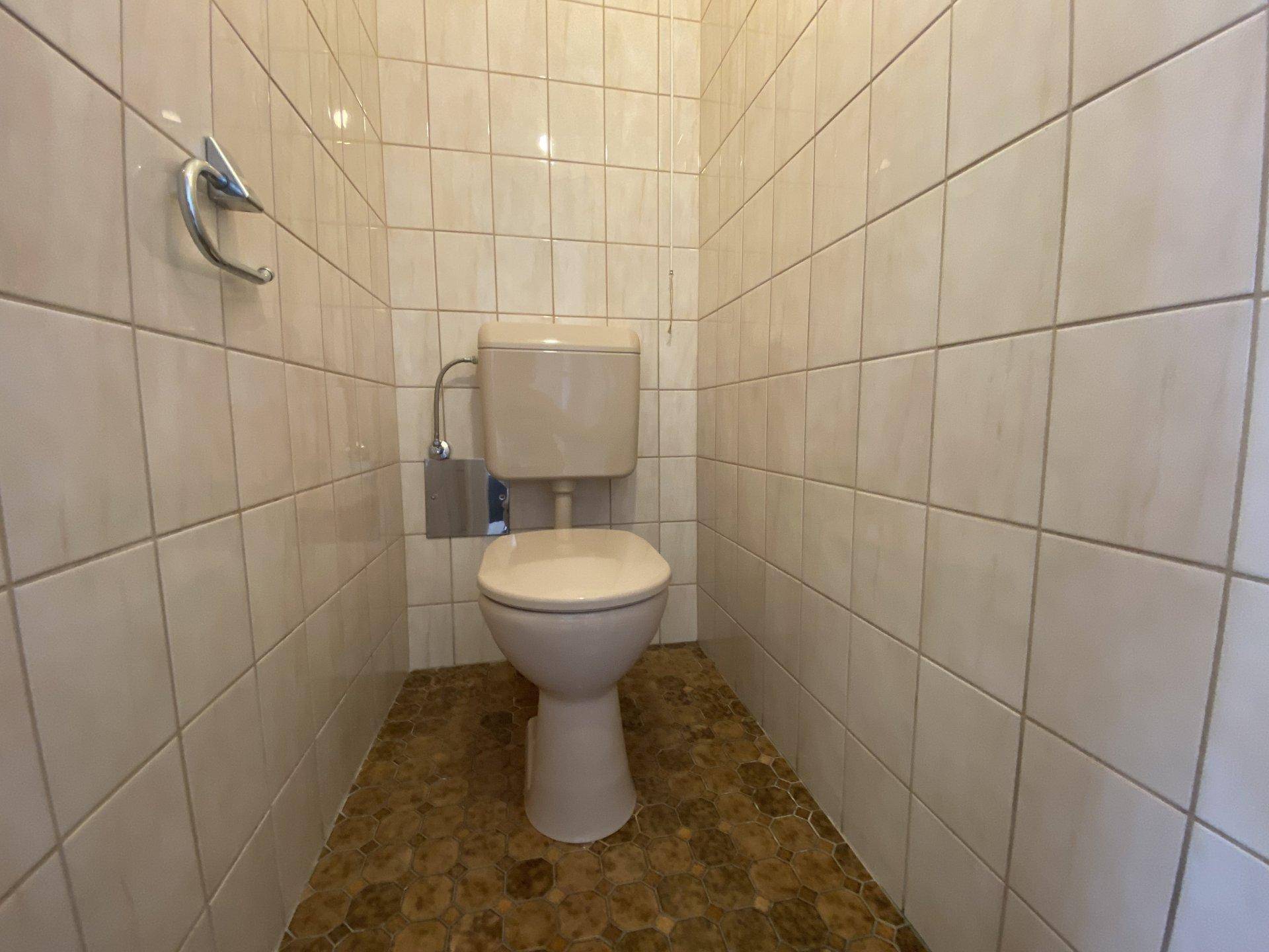 Separates WC mit Toilette und hellen Fliesen an Wänden und Boden, funktional und sauber.