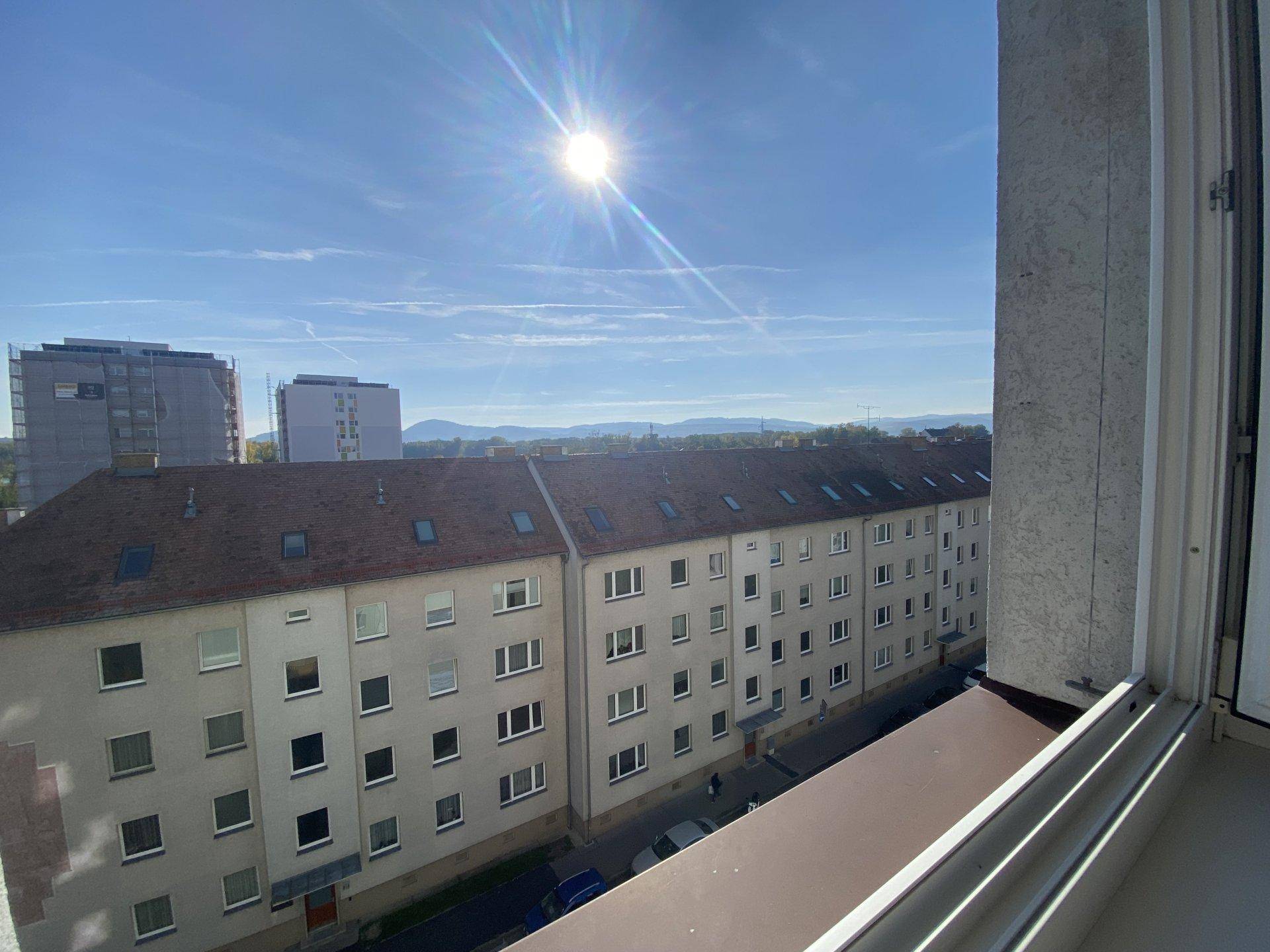 Sonniger Ausblick auf Wohngebäude, die Stadt und ferne Berge unter blauem Himmel.