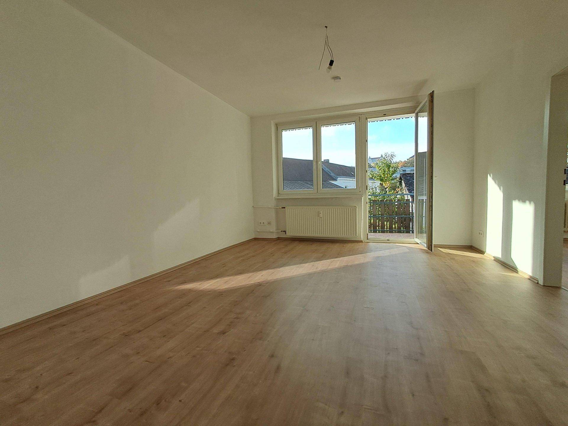 Geräumiges Wohnzimmer mit Laminatboden, viel Tageslicht und Zugang zum Balkon.