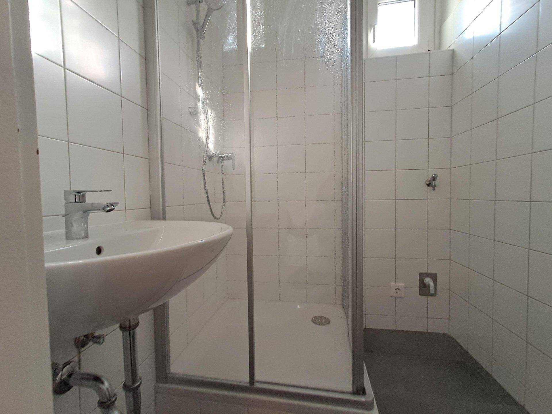 Funktionales Badezimmer mit Duschkabine, Waschbecken und weißen Fliesen.