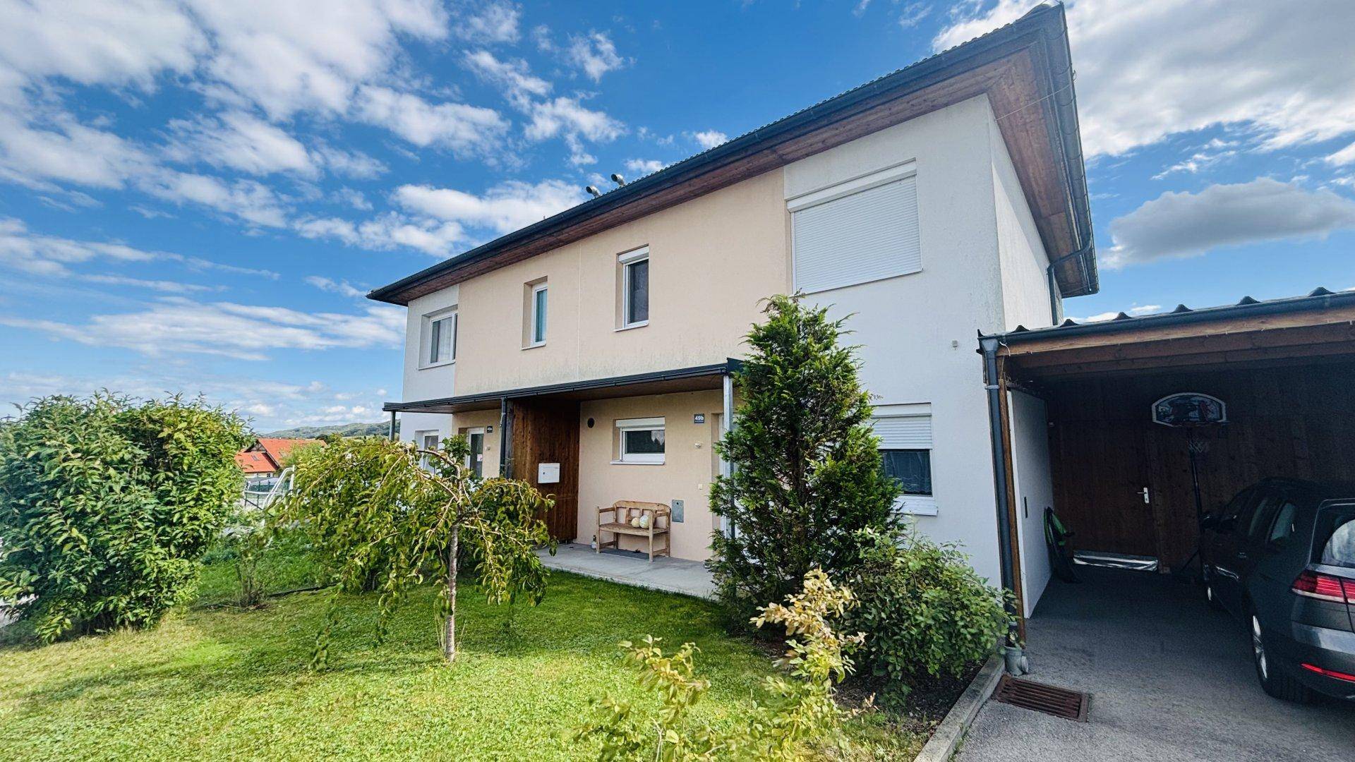 Doppelhaushälfte mit grünem Vorgarten und Carport unter einem bewölkten Himmel.