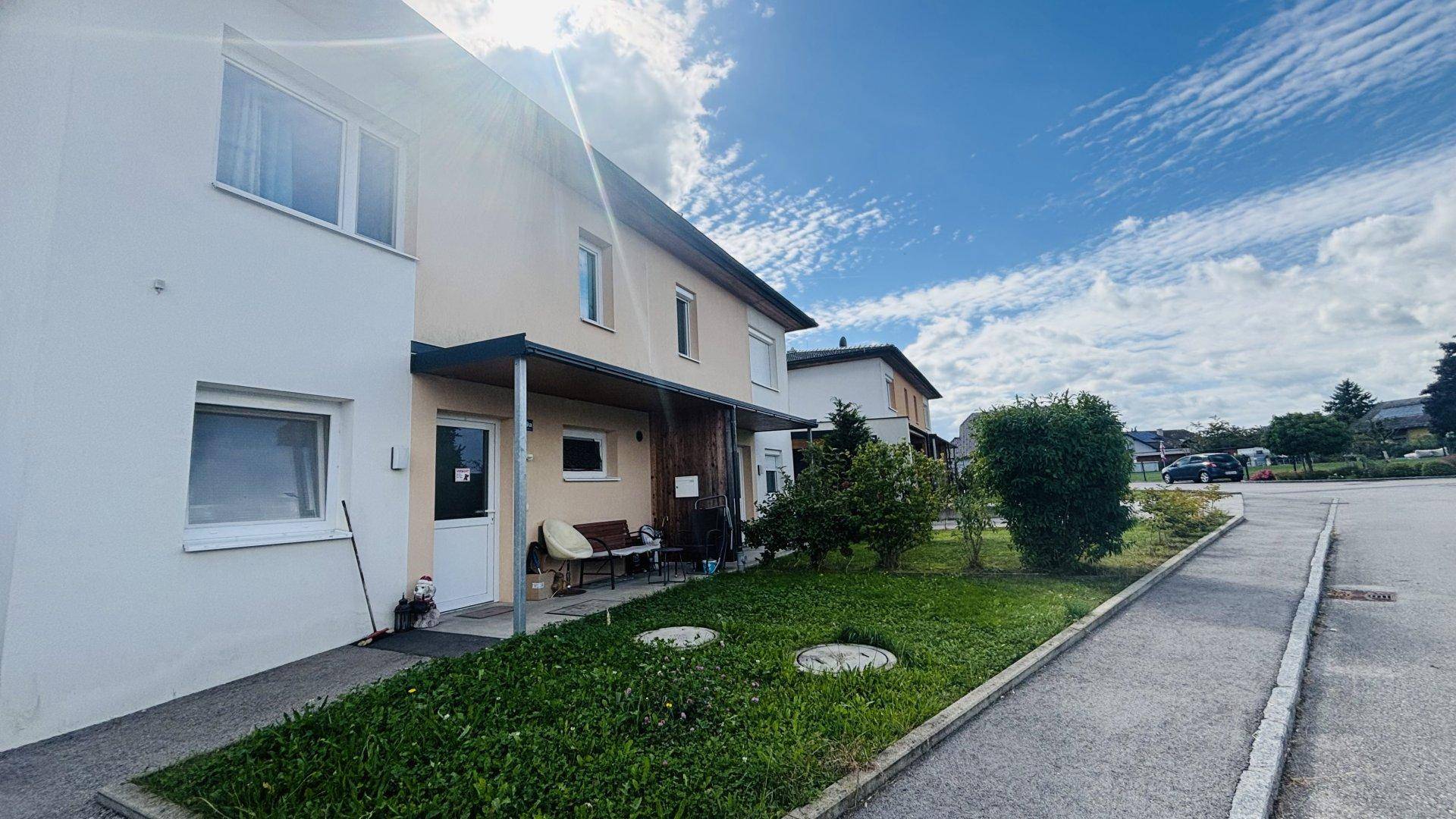 Seitenansicht der Doppelhaushälfte mit Eingangsbereich und angrenzender Straße bei Sonnenschein.