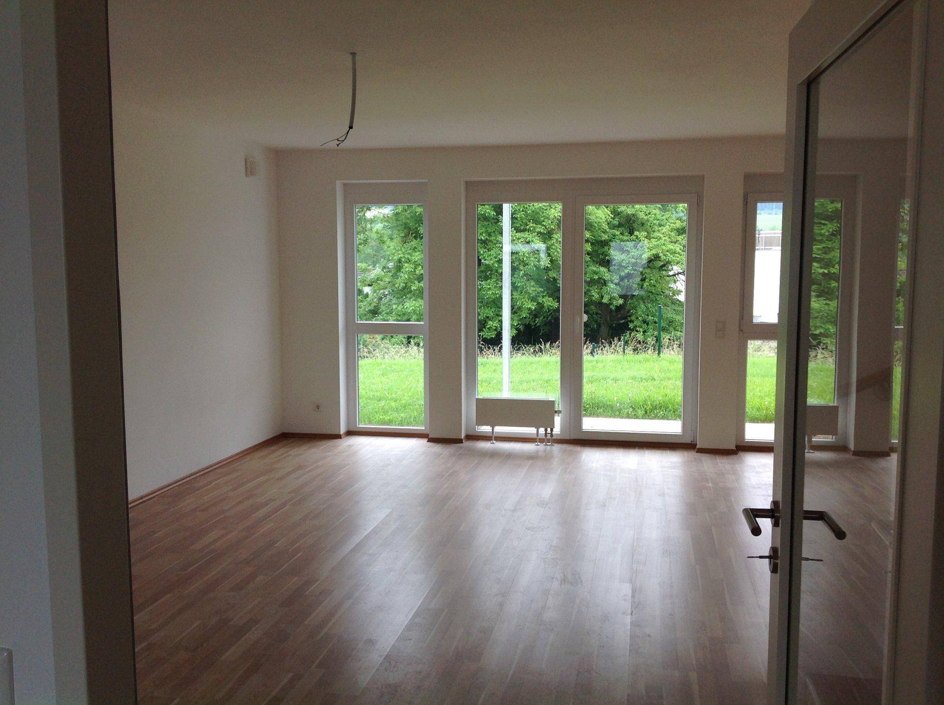 Heller, leerer Wohnraum mit Parkettboden und großen Fenstern zum Garten.
