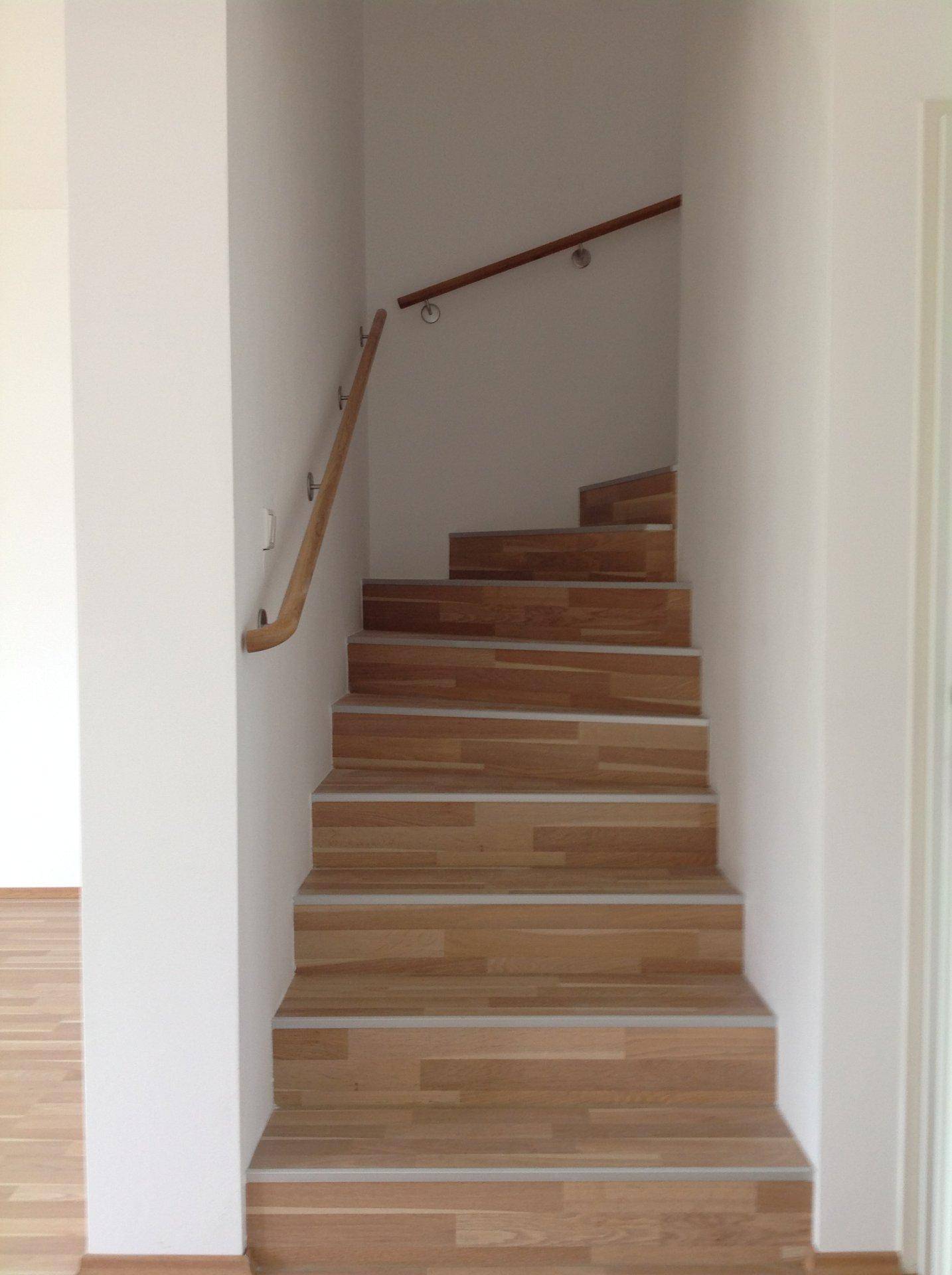 Holztreppe mit hellem Geländer, die in die obere Etage führt.