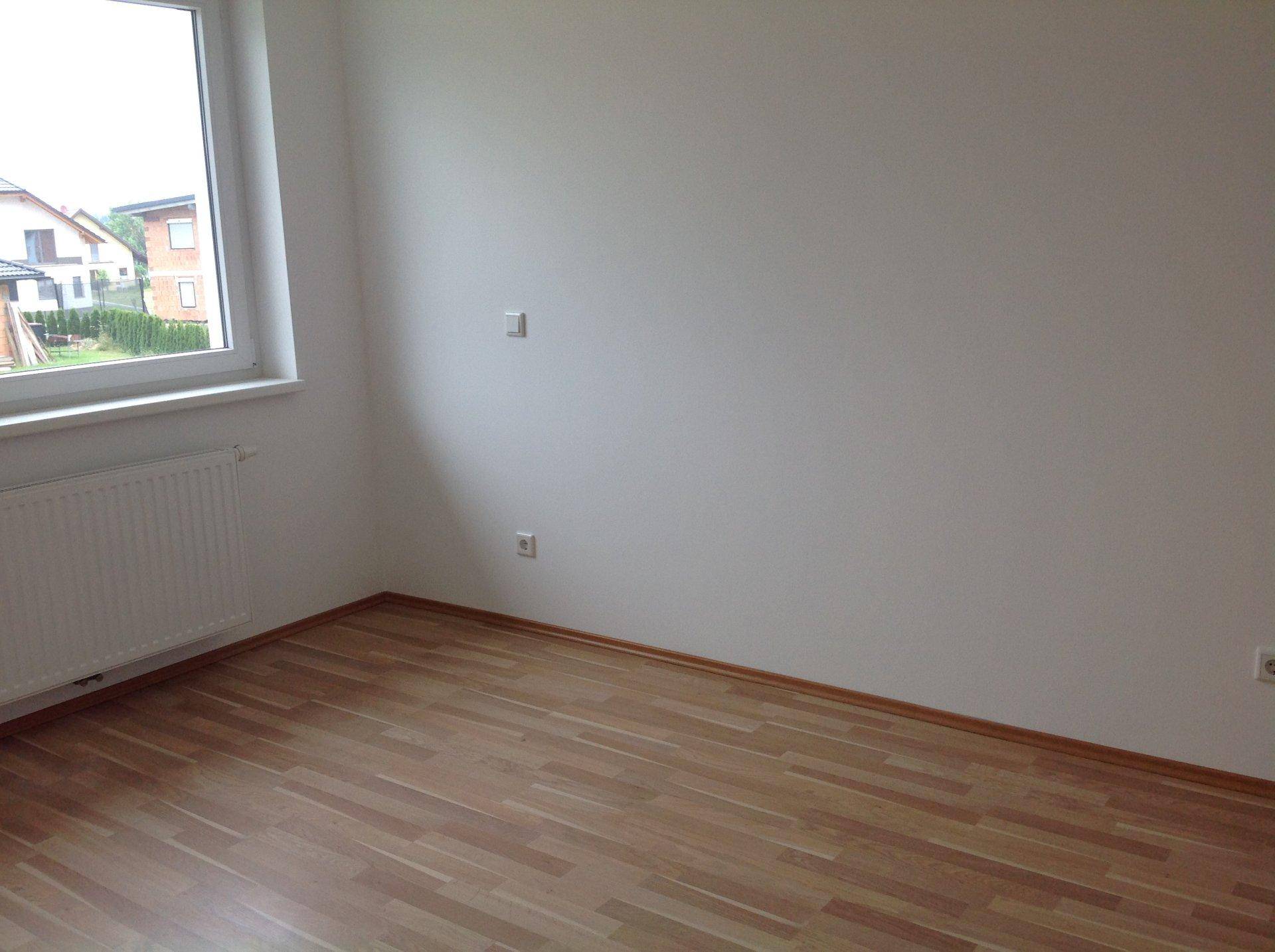 Leeres Zimmer mit Laminatboden, Heizkörper und Fenster mit Blick auf die Nachbarschaft.