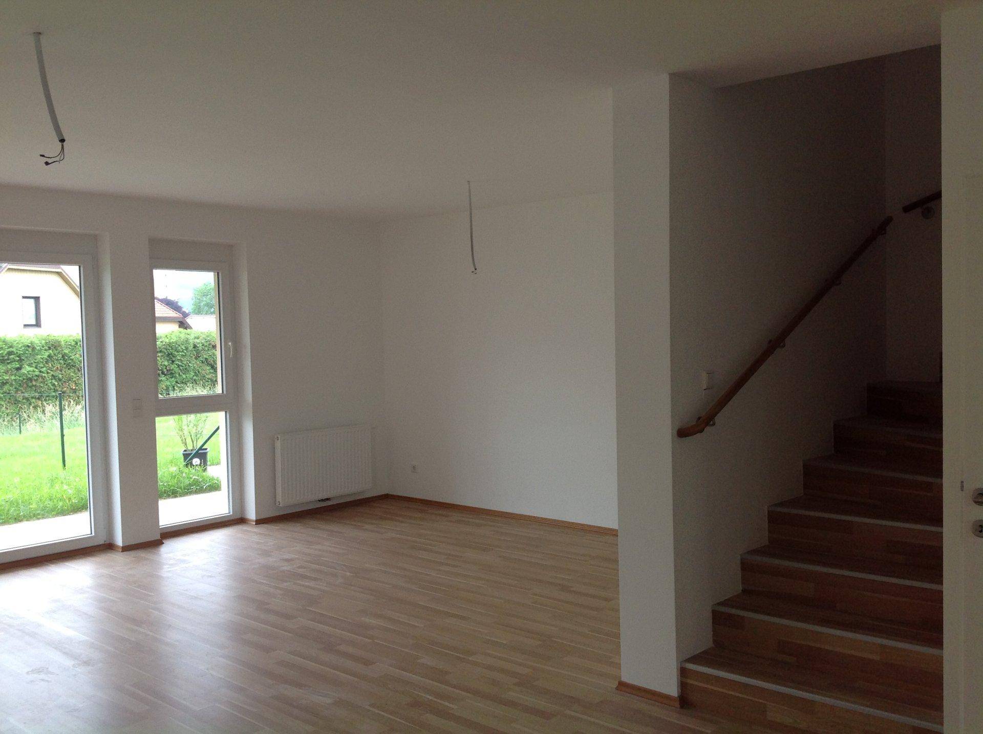 Geräumiger Wohnbereich mit Parkettboden, großen Fenstern und Zugang zur Treppe.