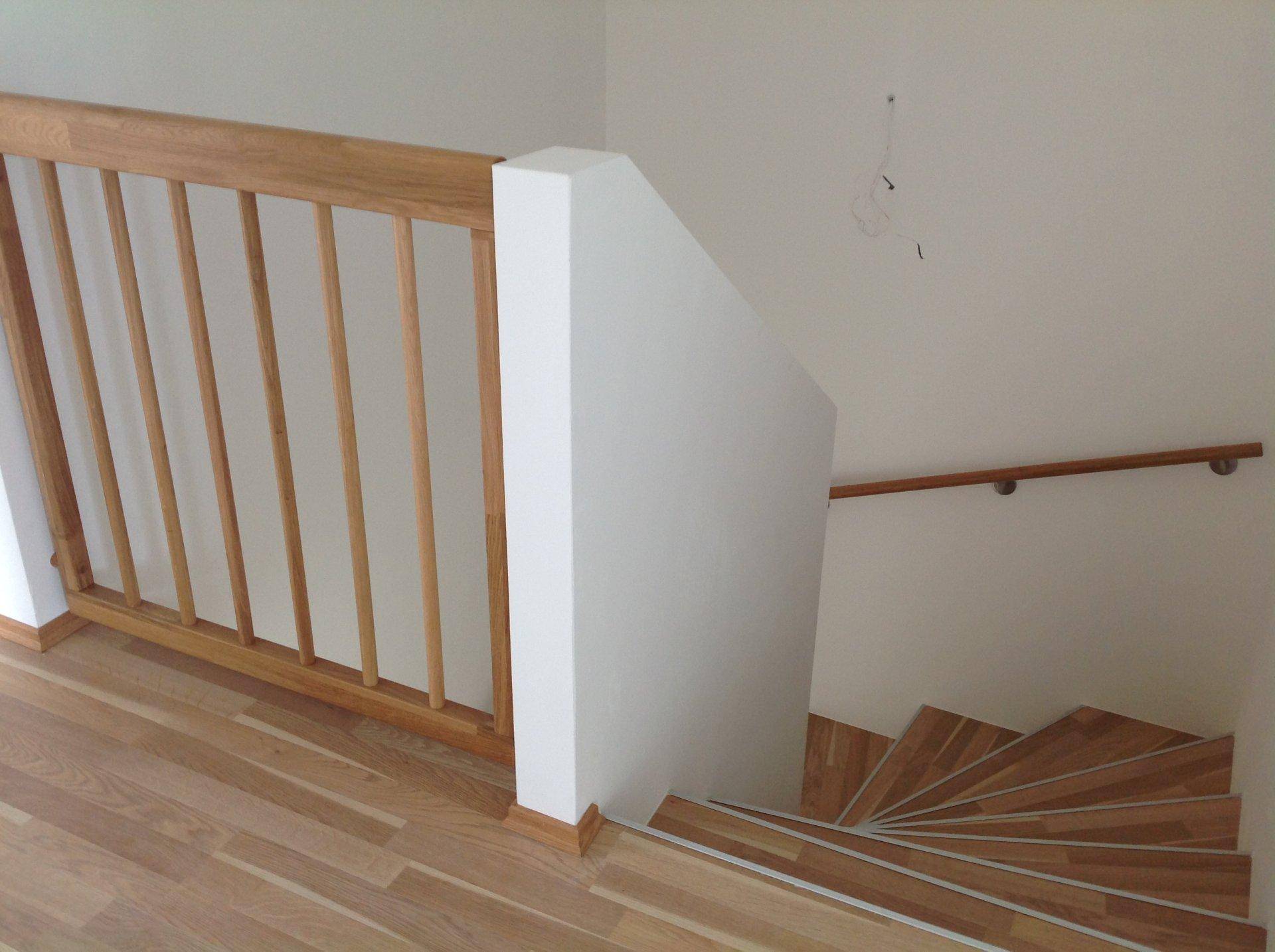Oberer Treppenabsatz mit Holzgeländer und Blick auf die darunterliegende Treppe.