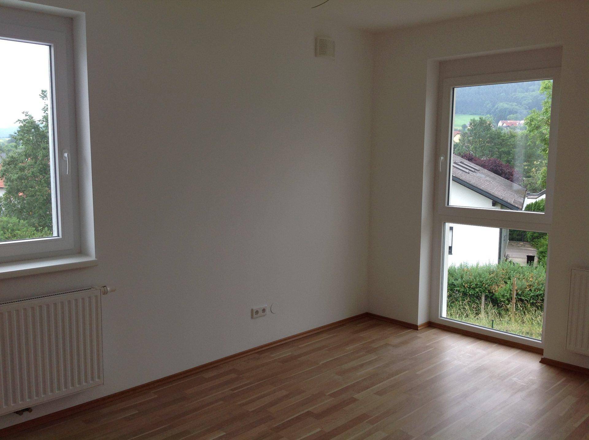 Geräumiges Zimmer mit Laminatboden und zwei Fenstern, die viel Tageslicht hereinlassen.