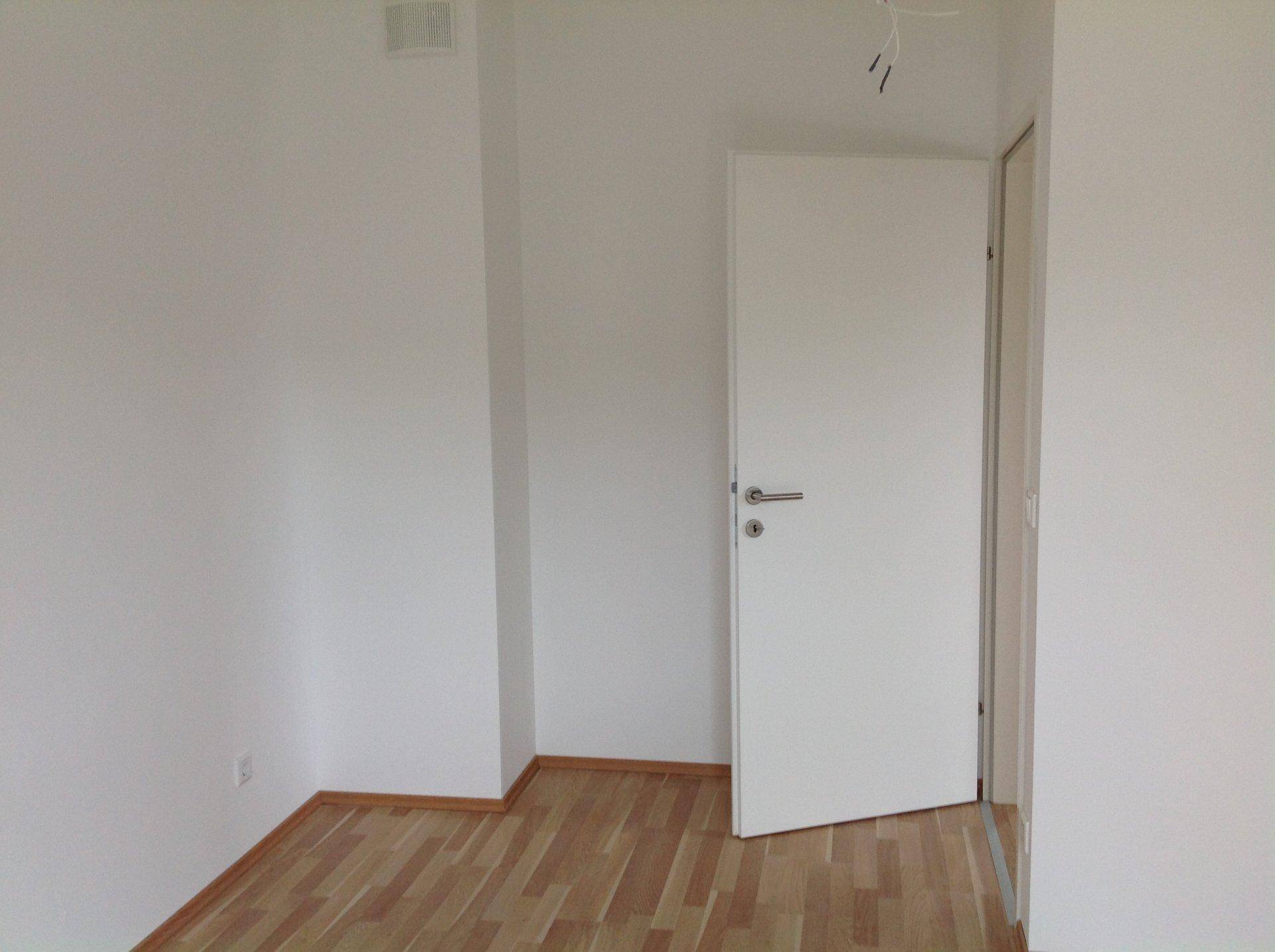 Leeres Zimmer mit Laminatboden und einer weißen Tür, bereit zur individuellen Gestaltung.