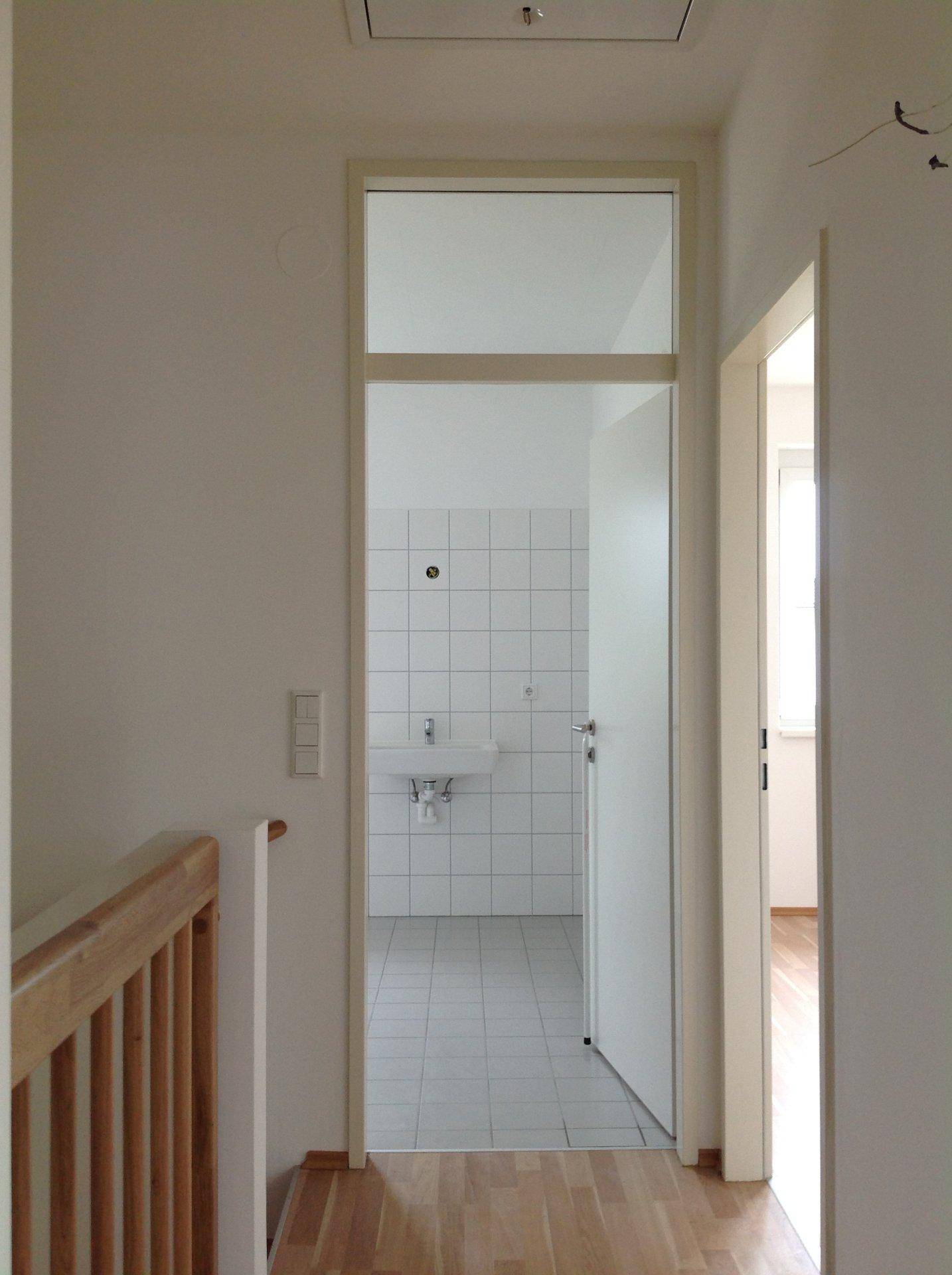 Heller Flur mit Holzboden, der zu einem Badezimmer mit weißen Fliesen führt.
