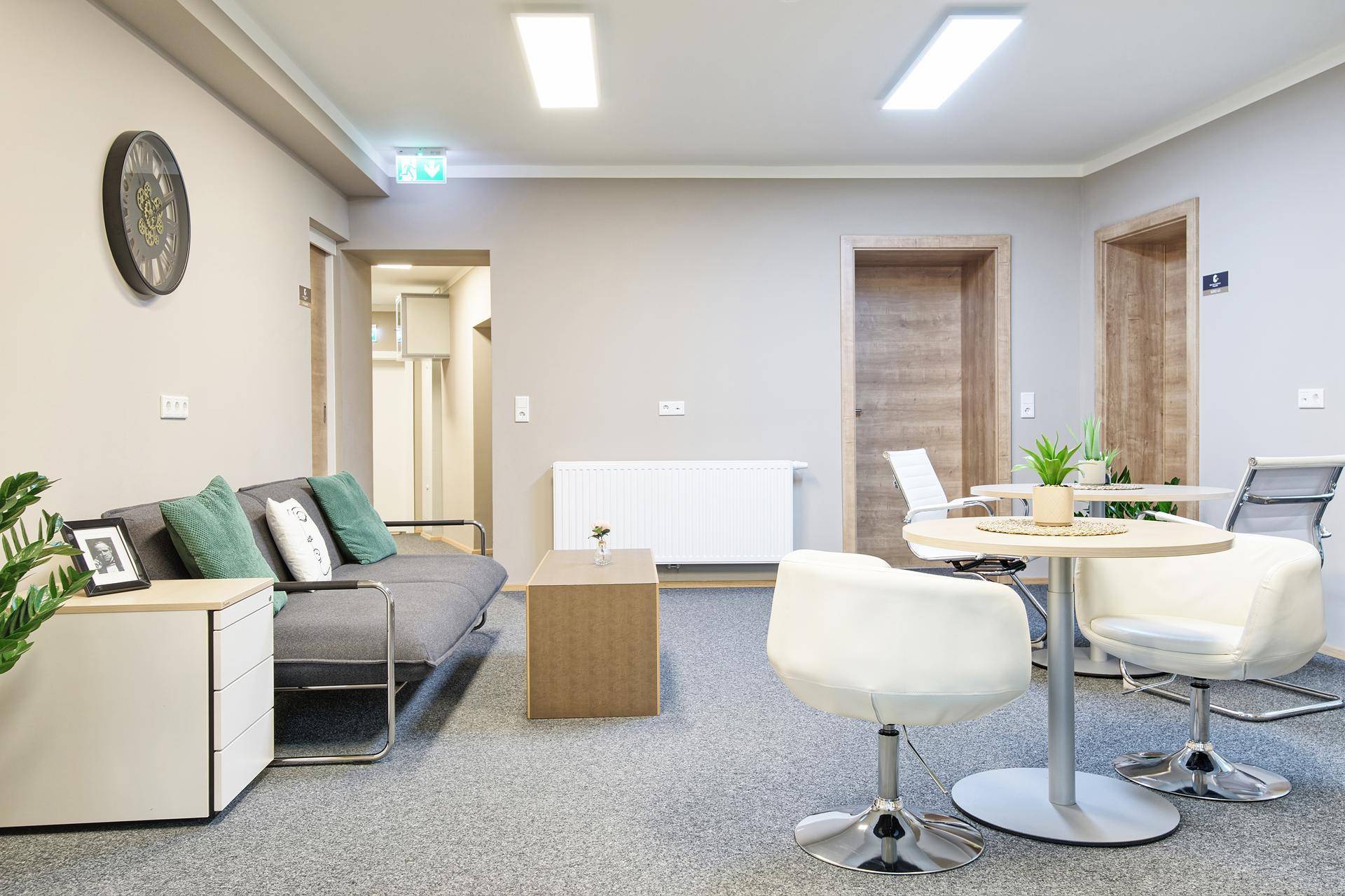 Gemütlicher Loungebereich mit Sofa, Couchtisch und kleinen Besprechungstischen auf Teppichboden.