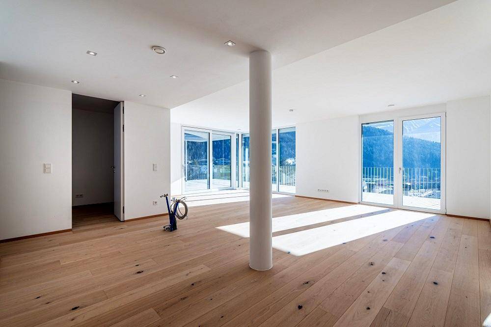 Lichtdurchfluteter Wohnbereich mit Eichenparkett, Säule und Zugang zu einer großen Terrasse.