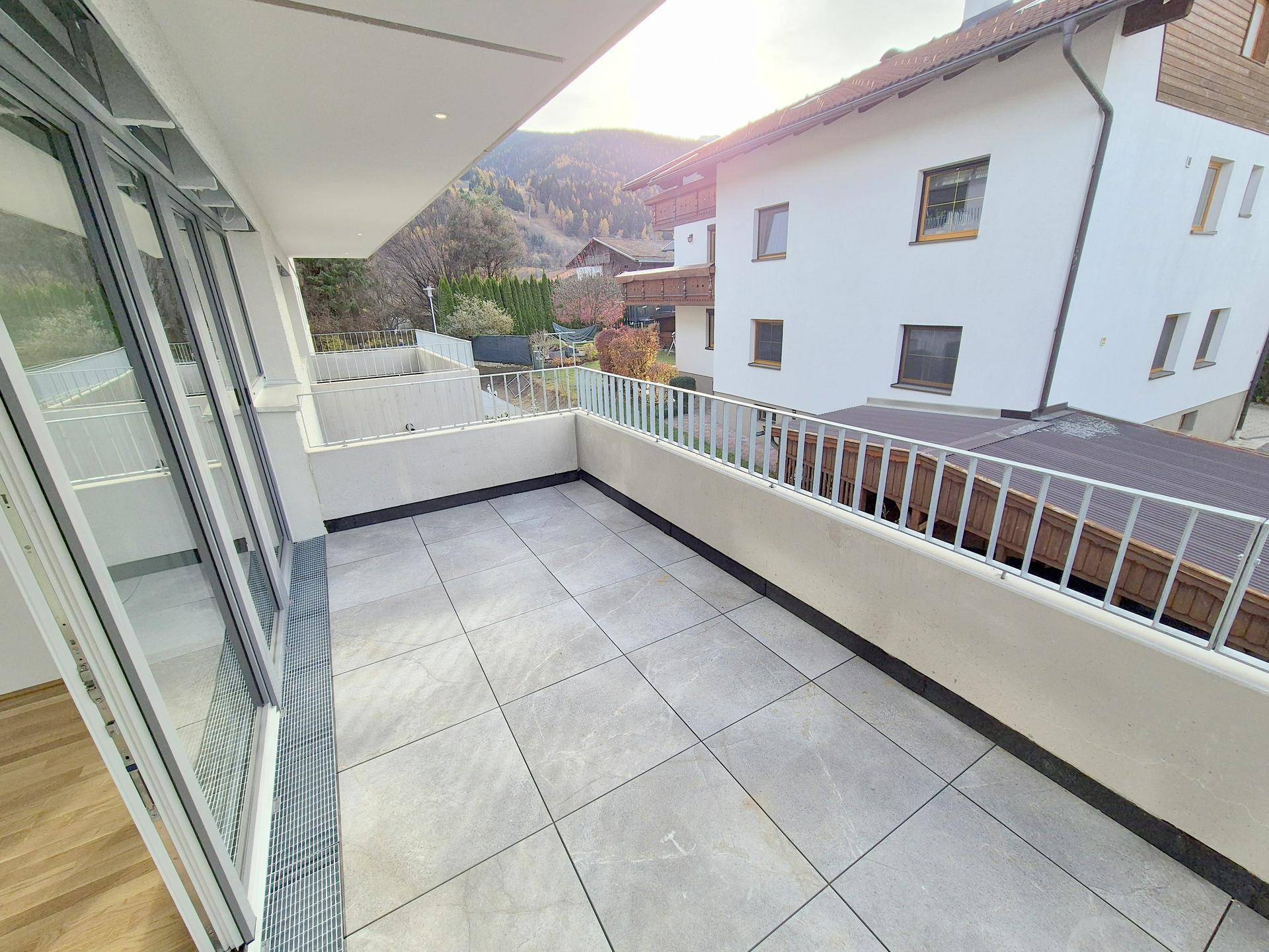 Geräumiger Balkon mit modernen Fliesen und Blick auf die umliegende Bebauung und Berge.