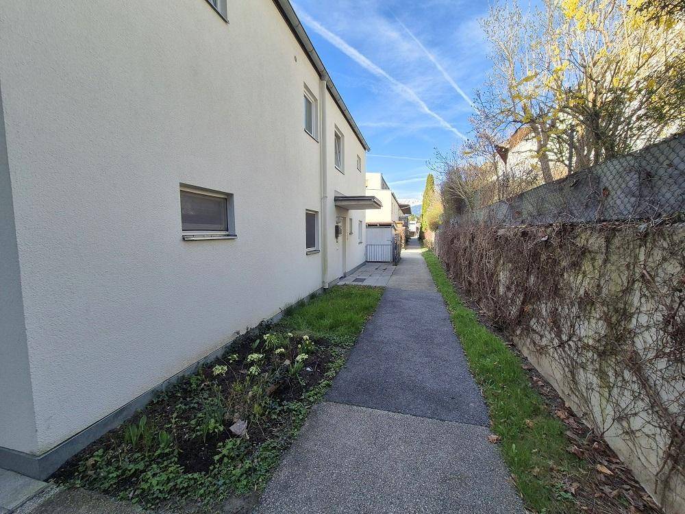Seitenansicht des Gebäudes mit einem gepflasterten Weg und Blumenbeeten.