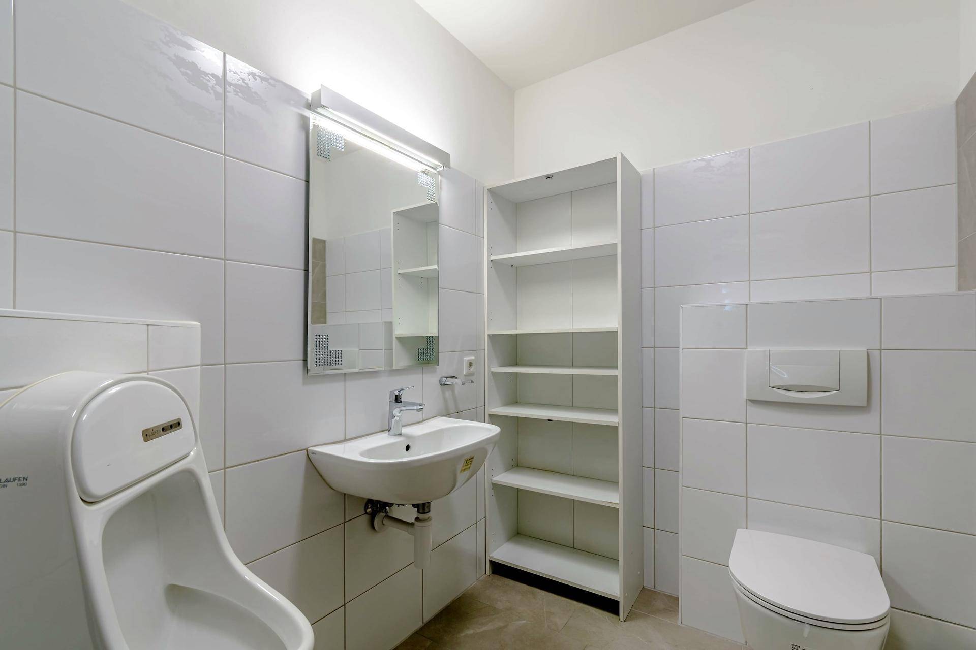 Helles Badezimmer mit weißen Fliesen, Urinal, Waschbecken und Toilette, funktional eingerichtet.