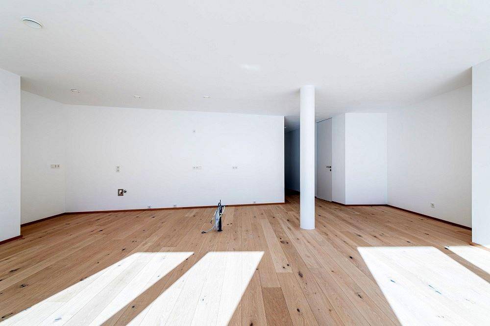 Geräumiger, unmöblierter Wohnbereich mit weiß gestrichenen Wänden und hellem Holzboden.