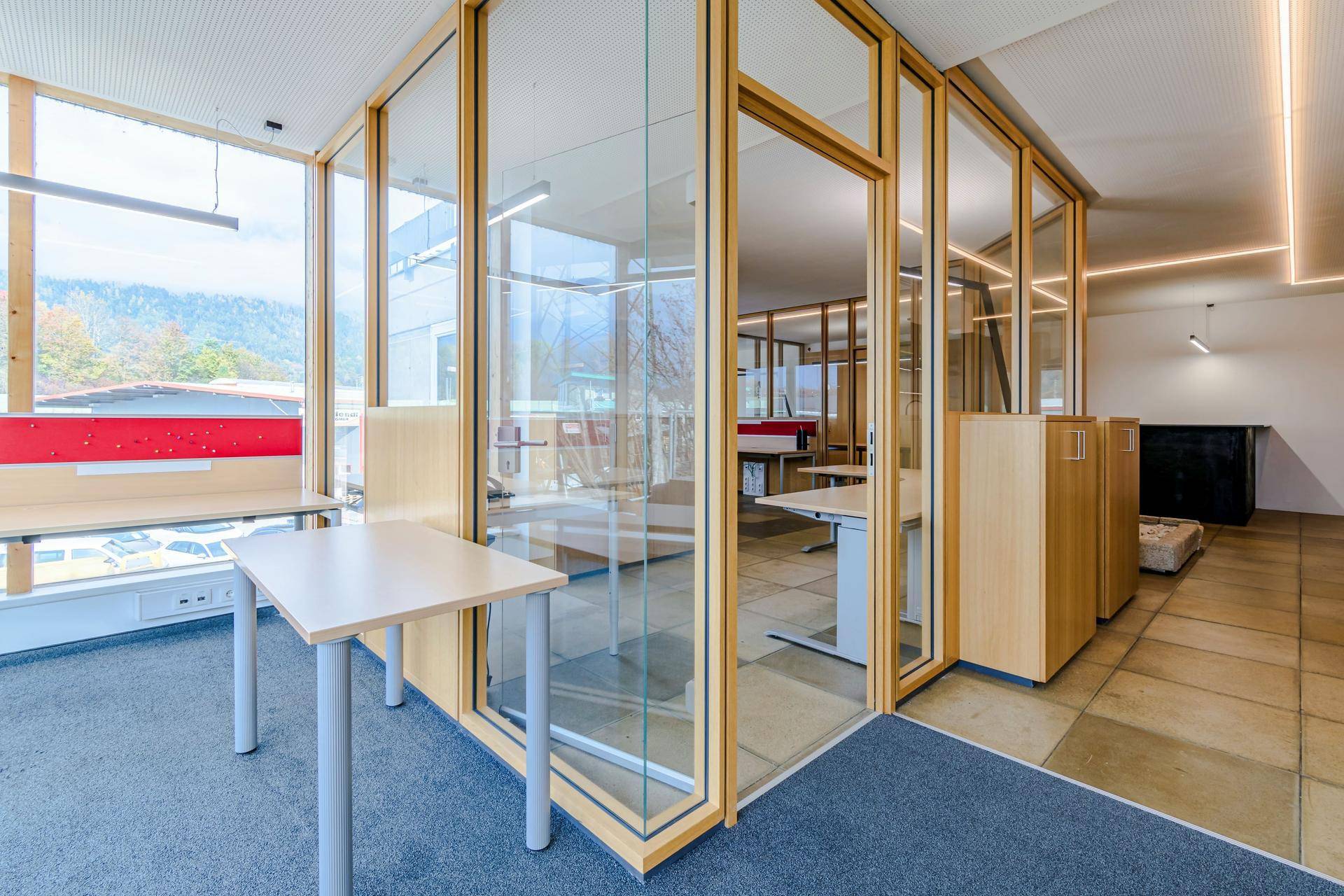 Heller Bürobereich mit Teppichboden, Glaswänden und Blick auf die umliegende Landschaft.