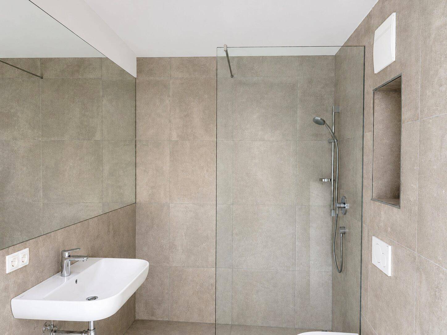 Modernes Badezimmer mit beigefarbenen Fliesen, bodengleicher Dusche und Einzelwaschbecken.