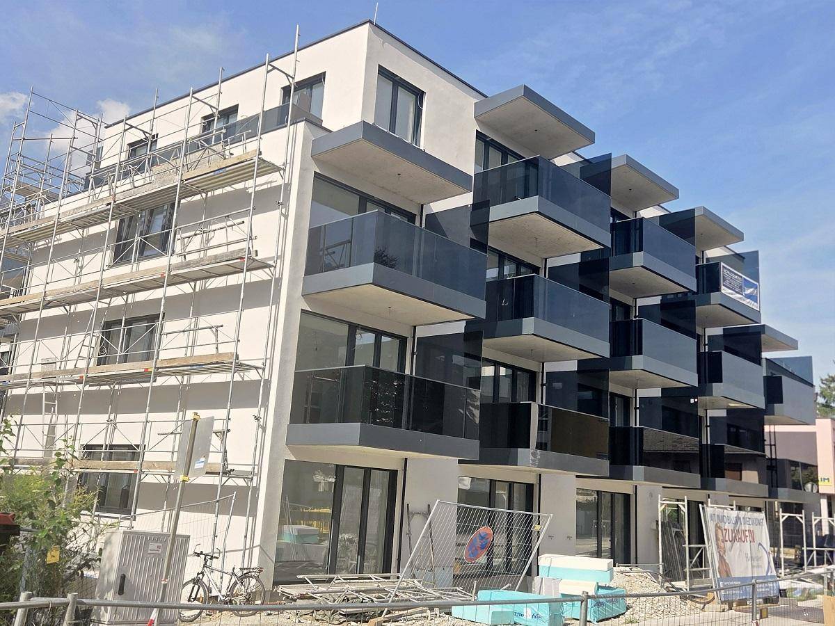Modernes Apartmentgebäude im Bau mit Gerüst, großen Fenstern und Balkonen mit Glasbrüstung.