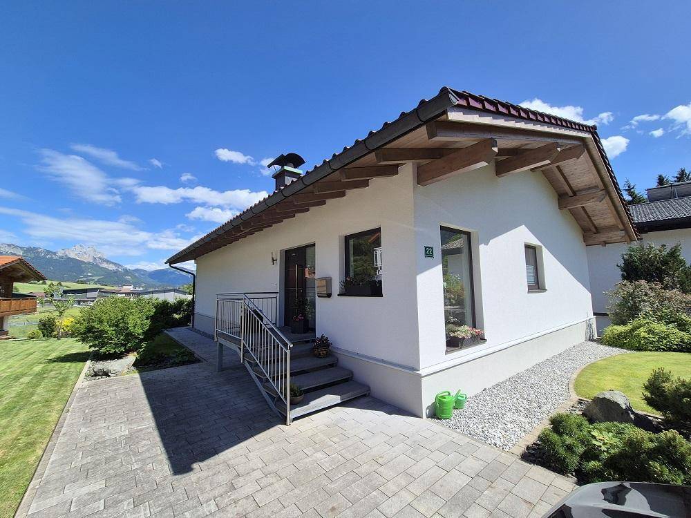Modernes Einfamilienhaus mit weißer Fassade, gepflastertem Eingang und weitem Bergblick.