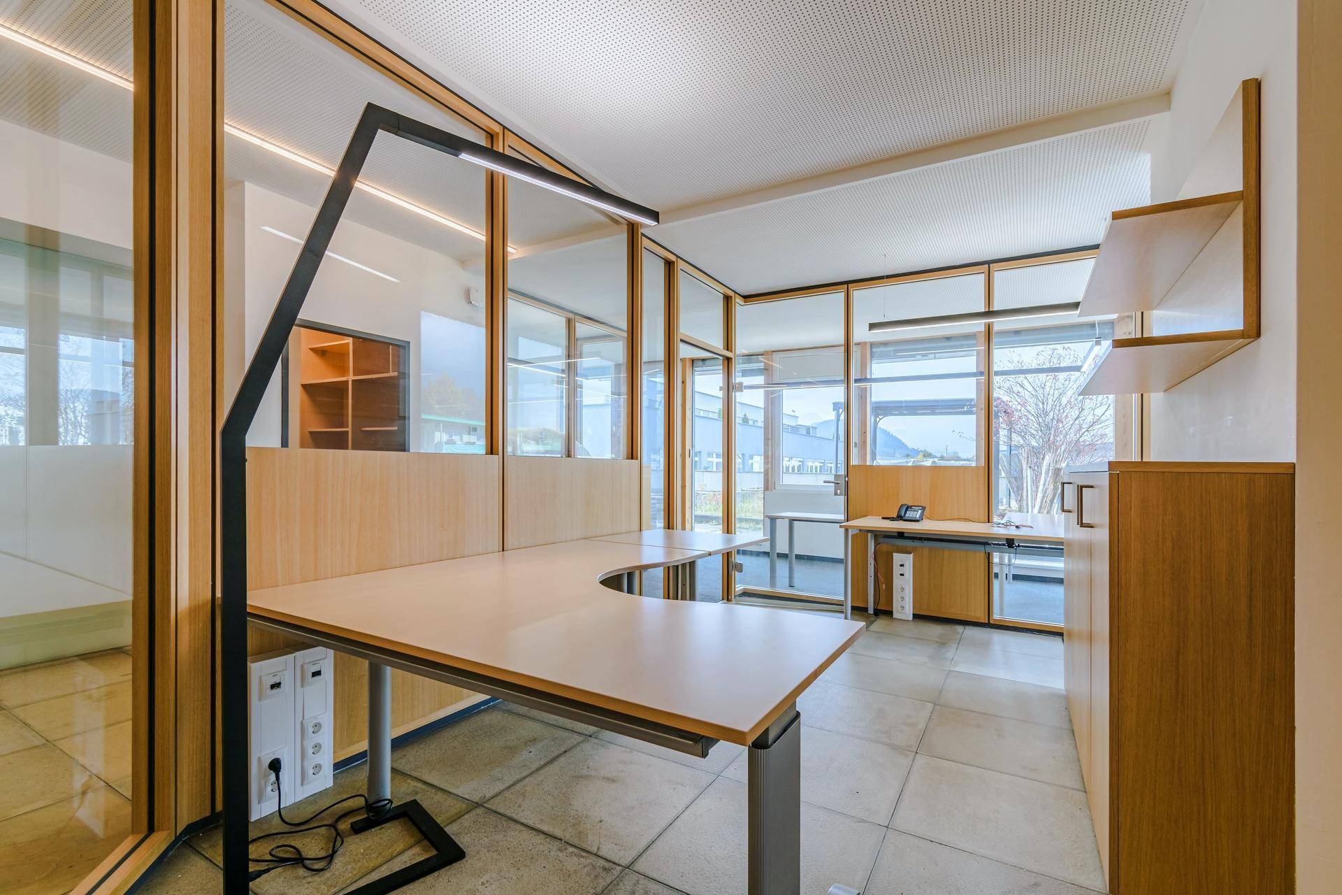 Heller Bürobereich mit ergonomischem Schreibtisch, Glaswänden und Blick auf die Umgebung.