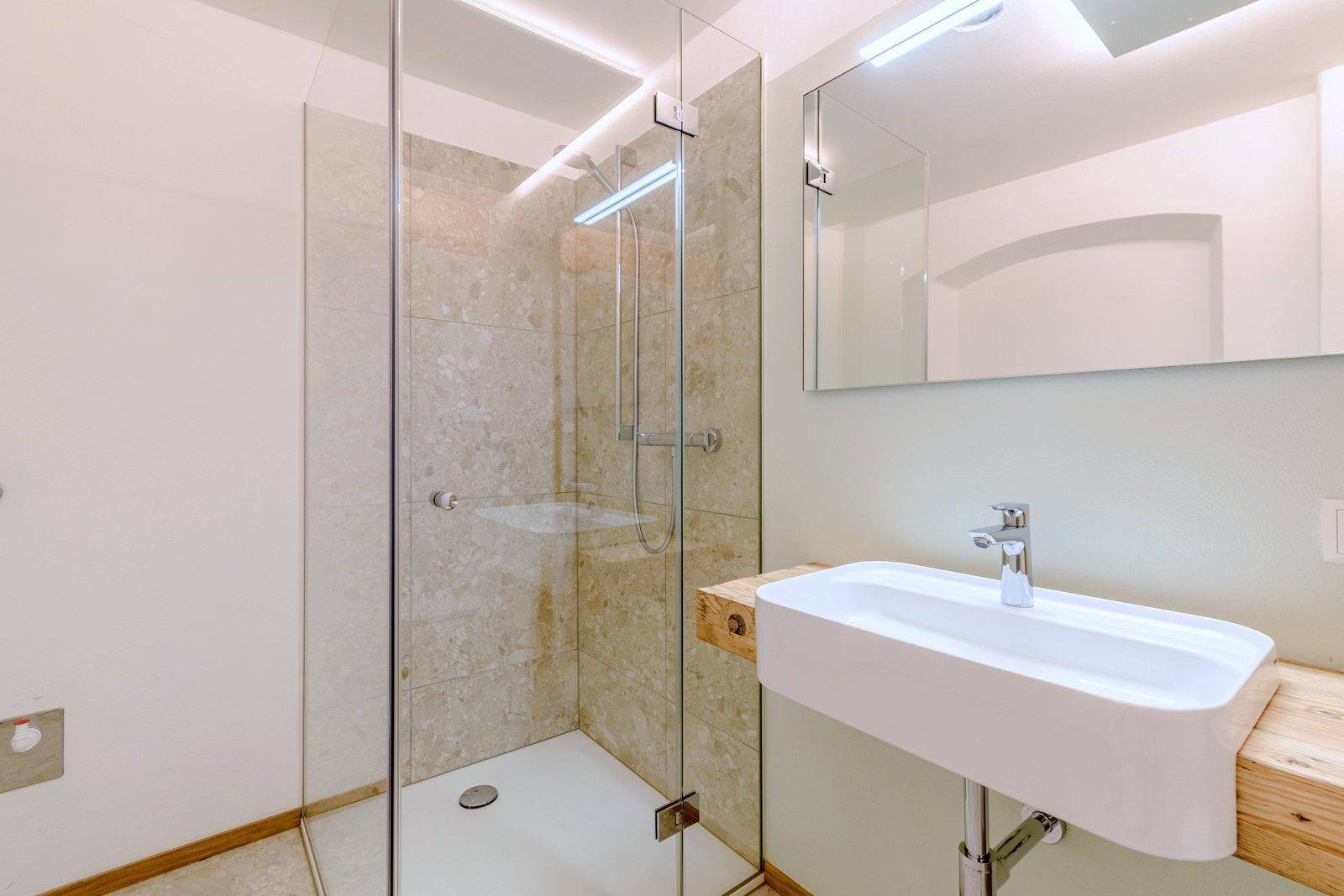 Modernes Badezimmer mit begehbarer Dusche, einem Waschbecken auf Holzplatte und hellen Fliesen an den Wänden.