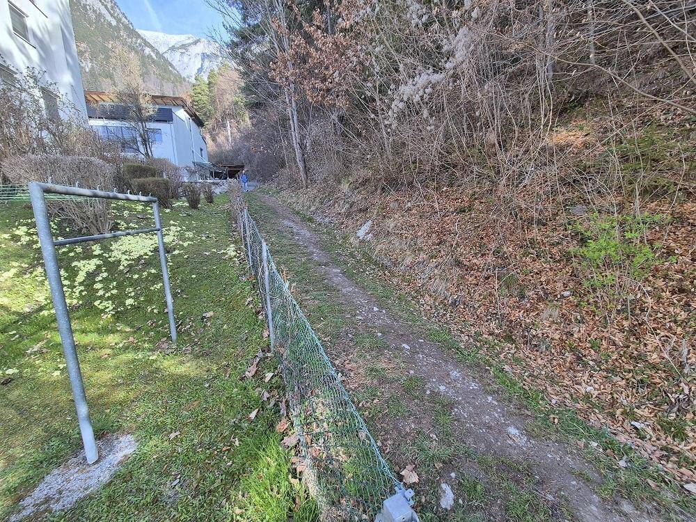 Schmaler Pfad entlang des Grundstücks, umgeben von natürlicher Vegetation.