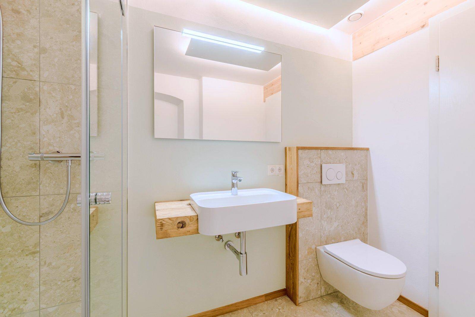 Modernes Badezimmer mit Waschbecken, Toilette und begehbarer Dusche, ergänzt durch helle Wände und Holzelemente.