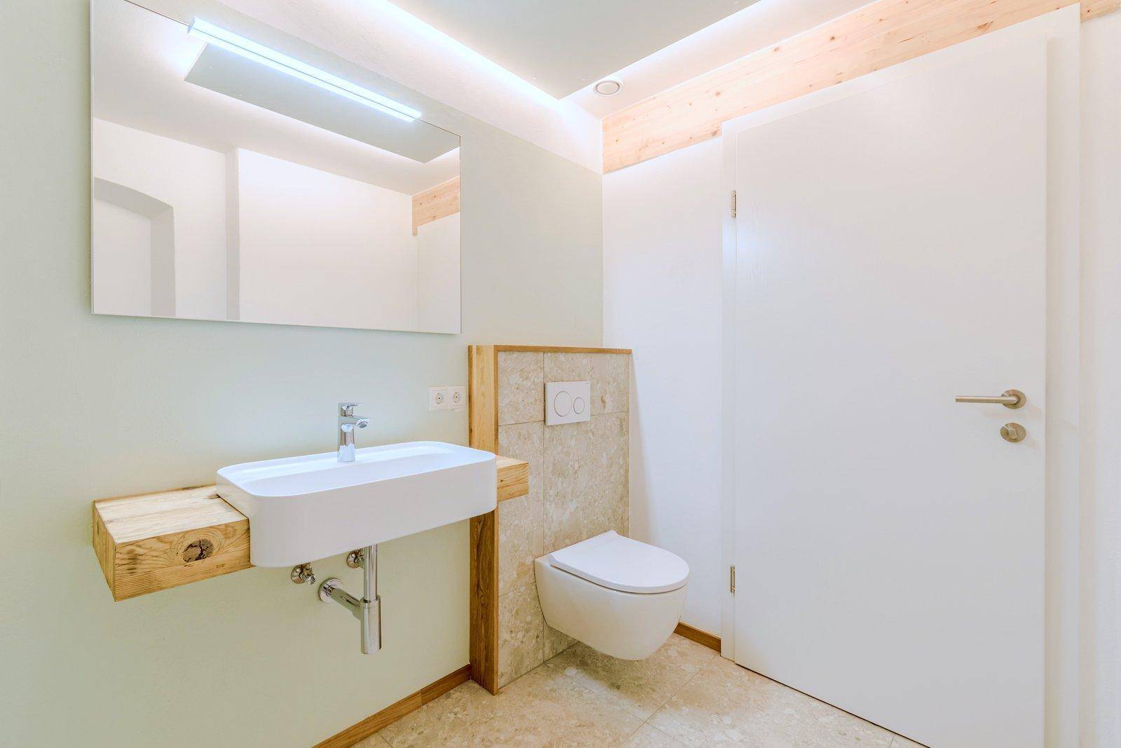 Modernes Badezimmer mit Waschbecken auf Holzkonsole und wandhängender Toilette, umgeben von hellen Fliesen.