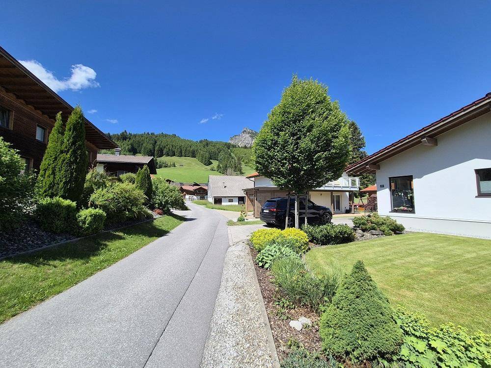 Idyllische Wohnstraße mit gepflegten Gärten, Bäumen und beeindruckendem Bergblick.
