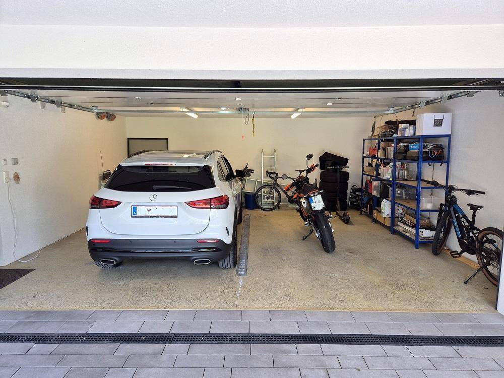 Geräumige Garage mit einem Auto, Motorrad, Fahrrädern und Lagerregalen.