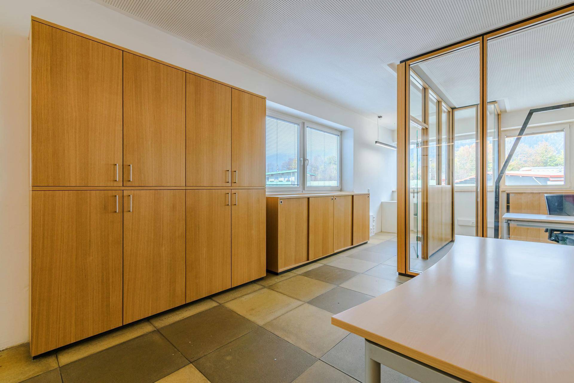 Geräumiger Bürobereich mit vielen Holzschränken für Stauraum und großen Fenstern.