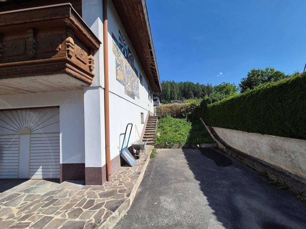 Seitenansicht des Hauses mit gepflastertem Weg, Treppe und einer hohen Hecke im Hintergrund.