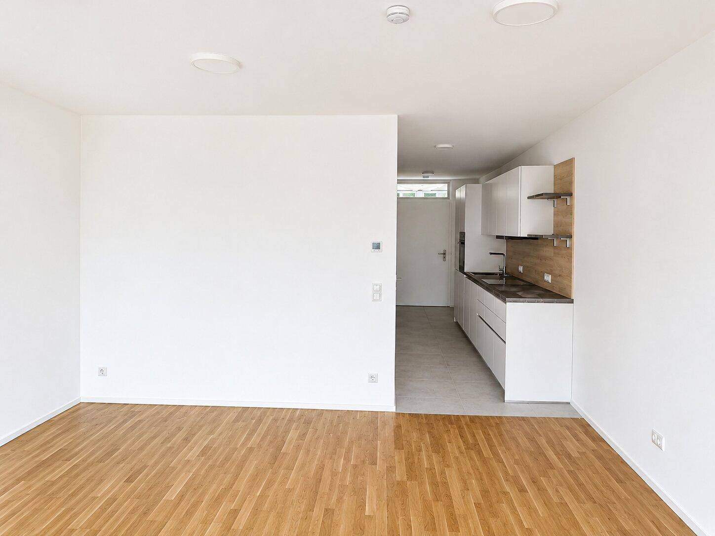 Offener Wohnbereich mit Holzboden und Blick auf die moderne, integrierte Küchenzeile.