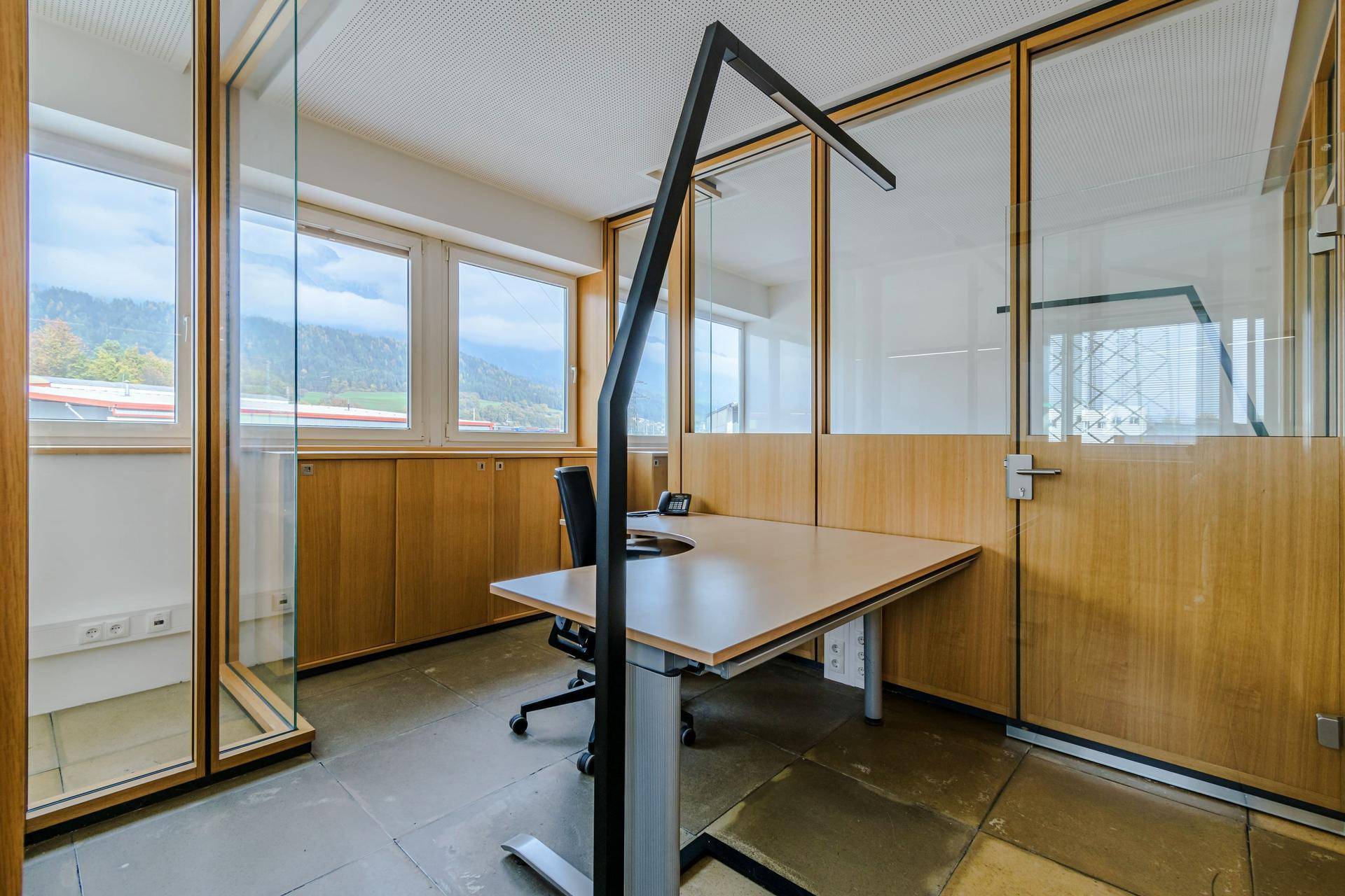 Einzelbüro mit ergonomischem Schreibtisch, großen Fenstern und Bergblick, durch Glaswände abgetrennt.