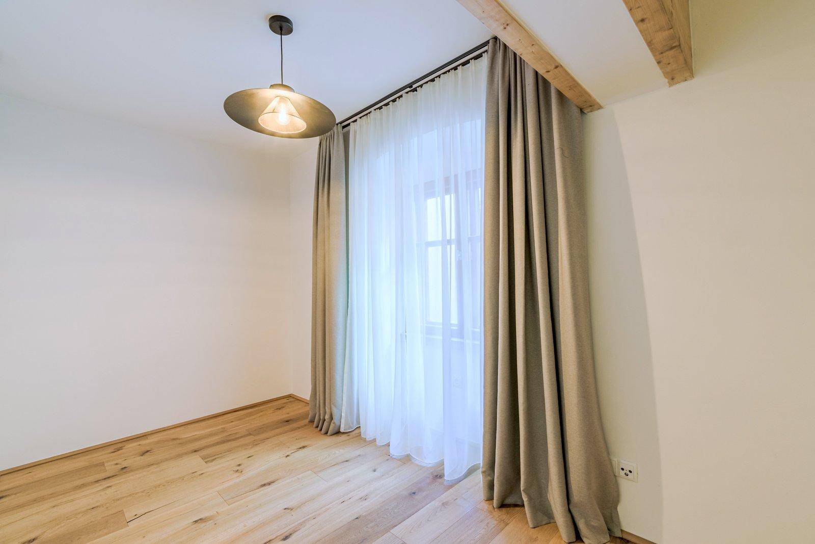 Gemütliches Schlafzimmer mit Holzboden, großem Fenster und einem sichtbaren Holzbalken an der Decke.