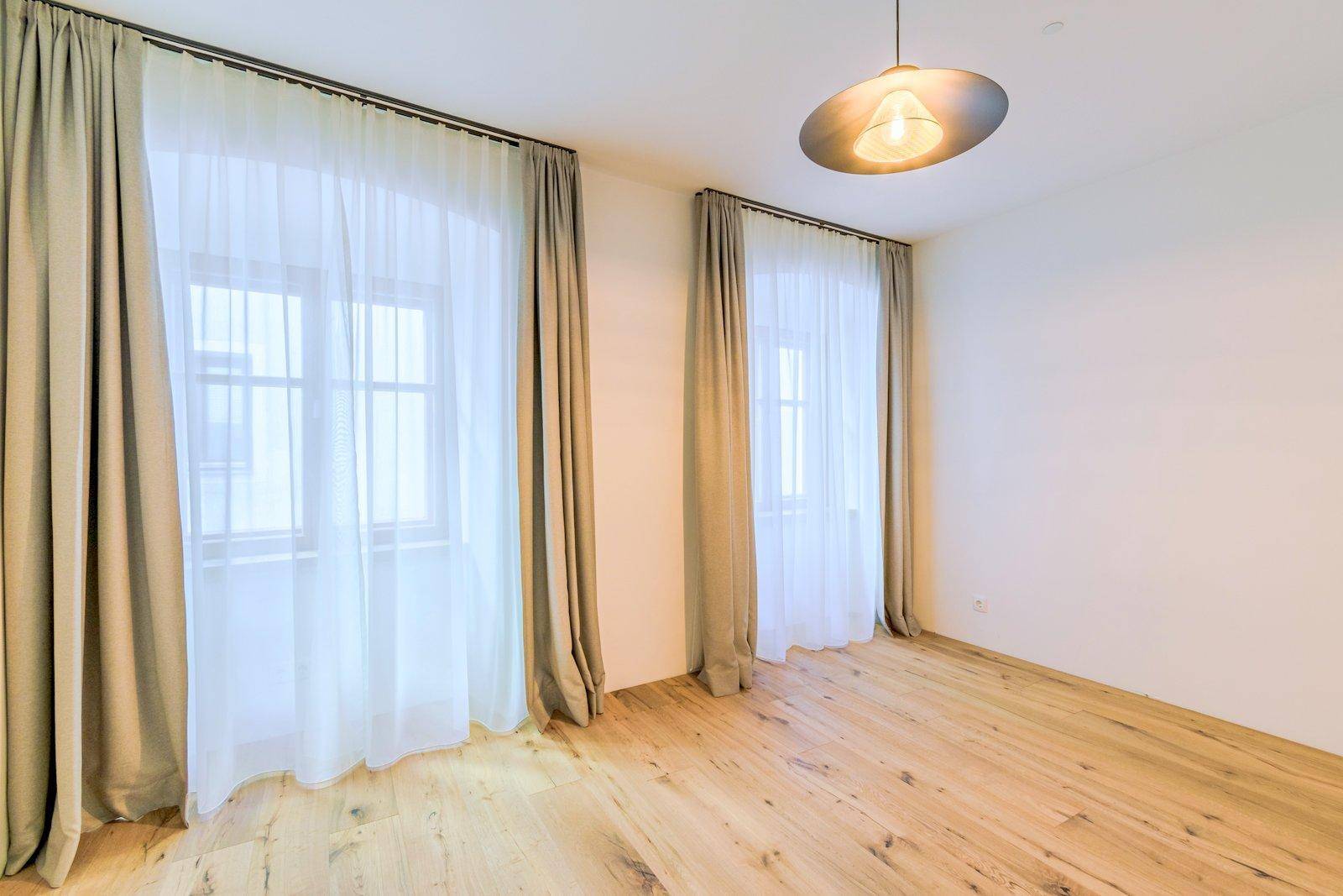 Helles Schlafzimmer mit Echtholzboden, zwei großen Fenstern und eleganten Vorhängen.