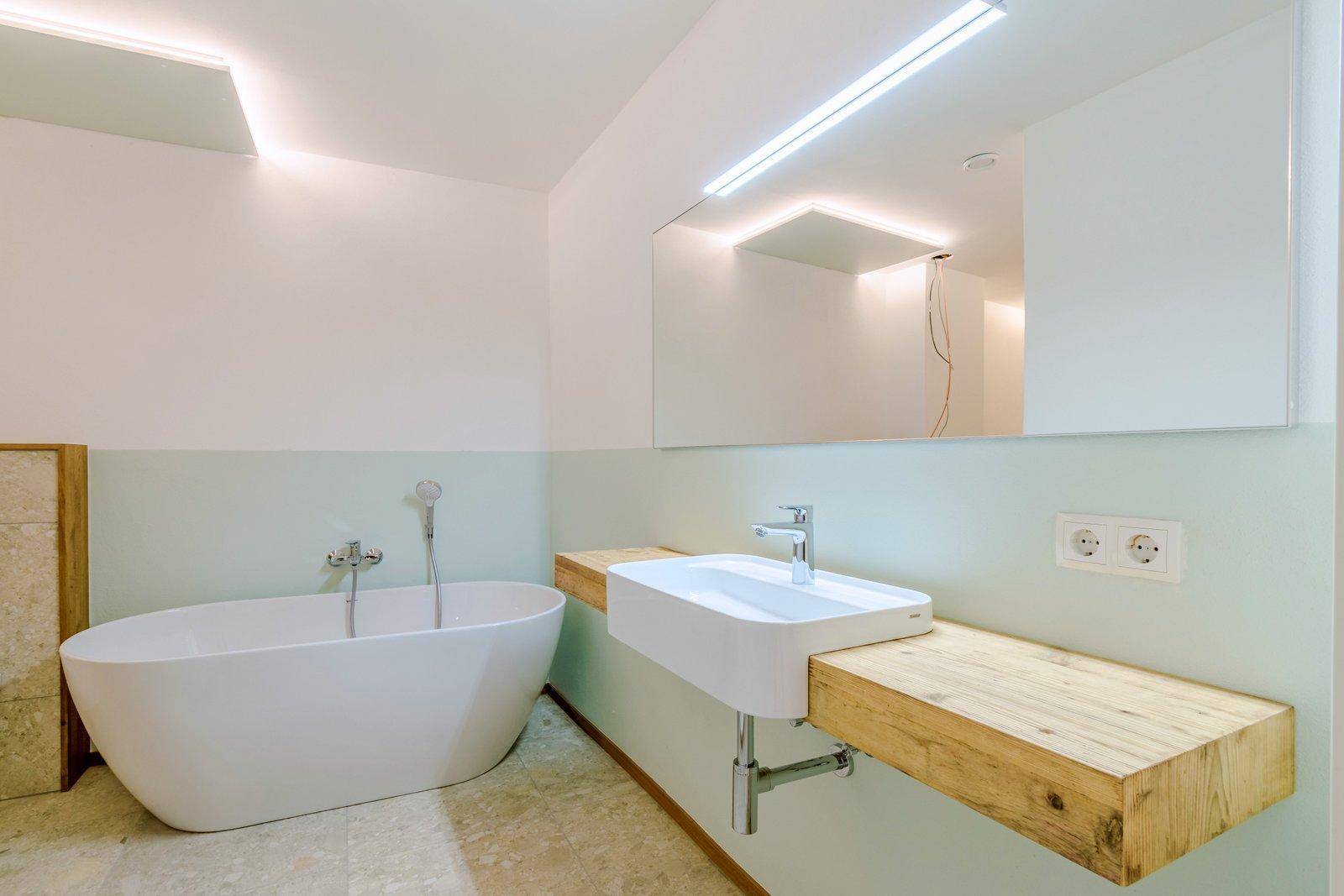 Helles Badezimmer im Bau mit freistehender Badewanne, modernem Waschbecken auf Holzplatte und großem Spiegel.