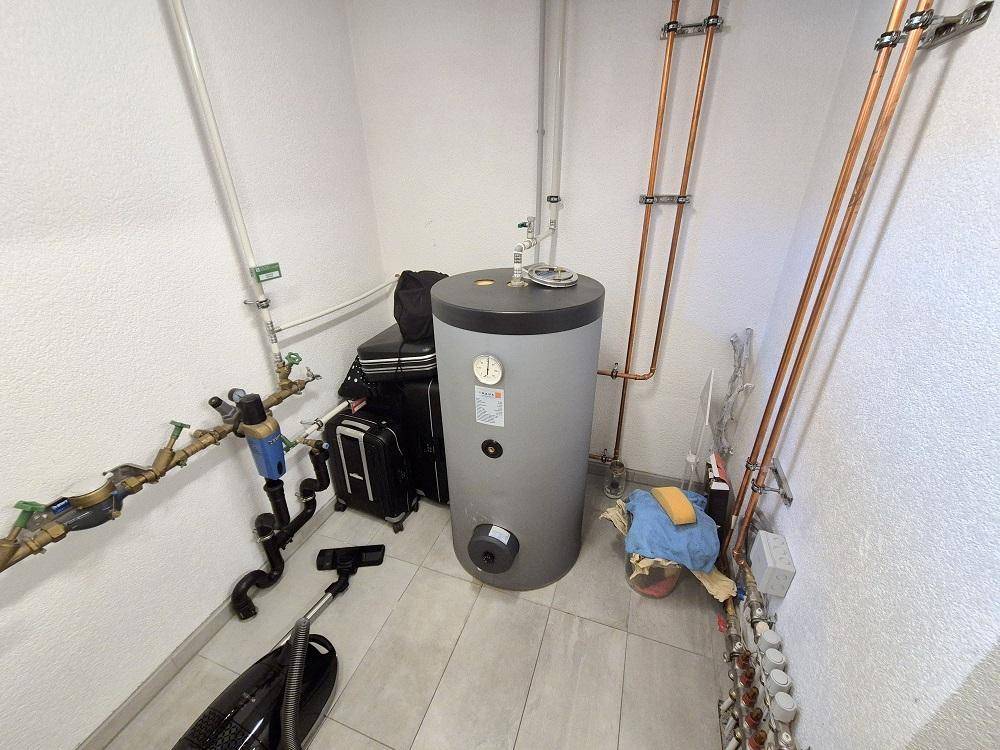 Hauswirtschaftsraum mit Warmwasserspeicher, sichtbaren Leitungen und Fliesenboden.