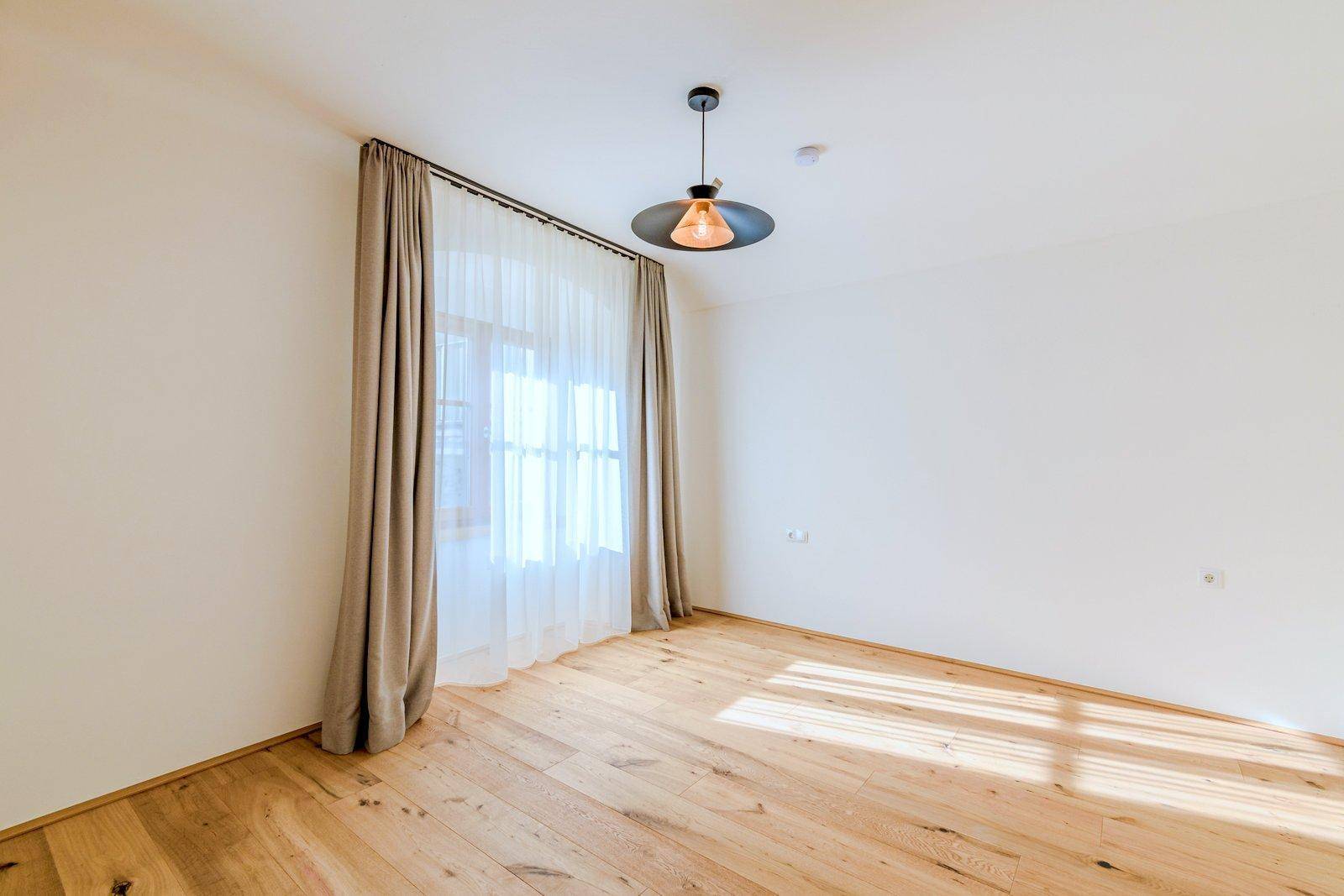 Geräumiges Zimmer mit Parkettboden und Vorhängen, das viel Sonnenlicht empfängt.