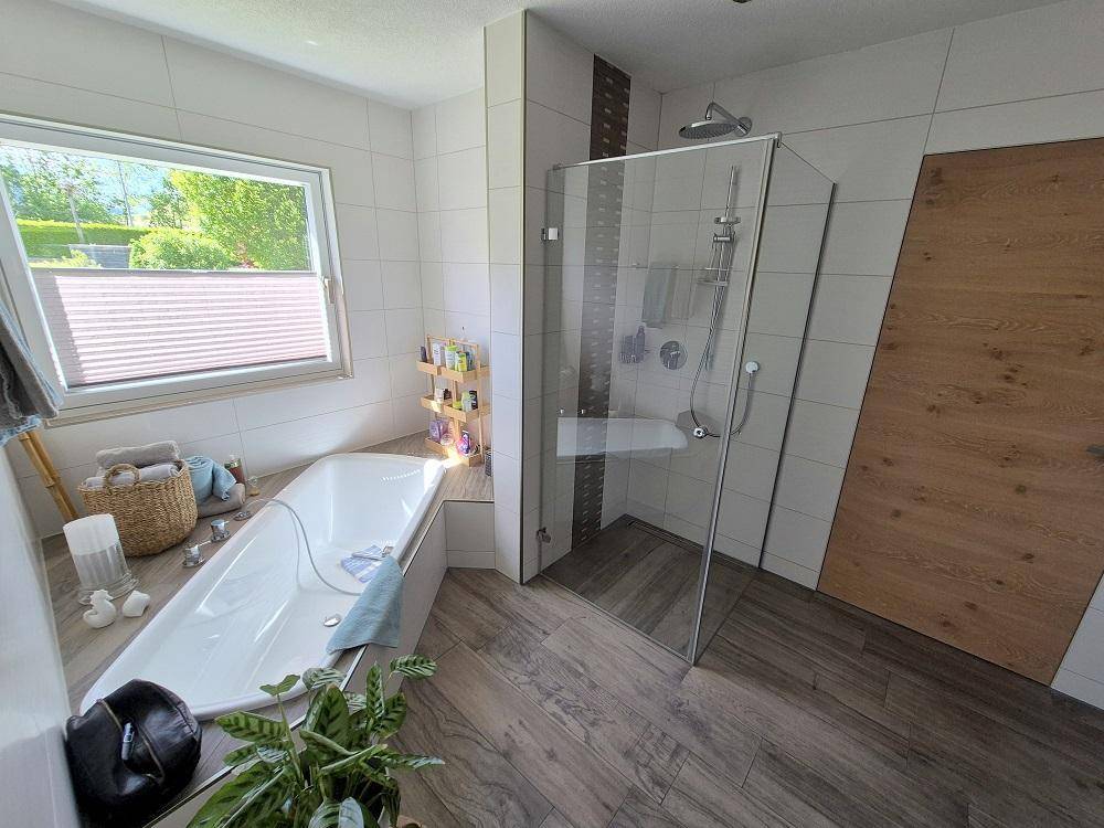 Modernes Badezimmer mit Badewanne, begehbarer Dusche und Holzoptik-Fliesenboden.