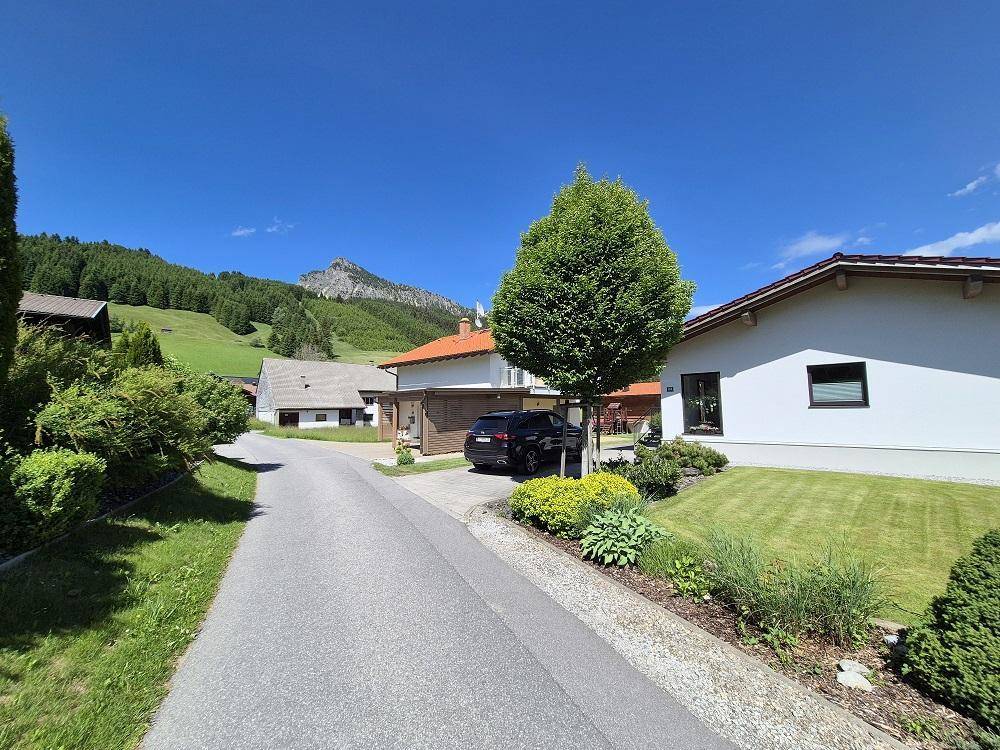 Ruhige Wohnstraße mit gepflegten Häusern, Gärten und malerischem Bergblick.