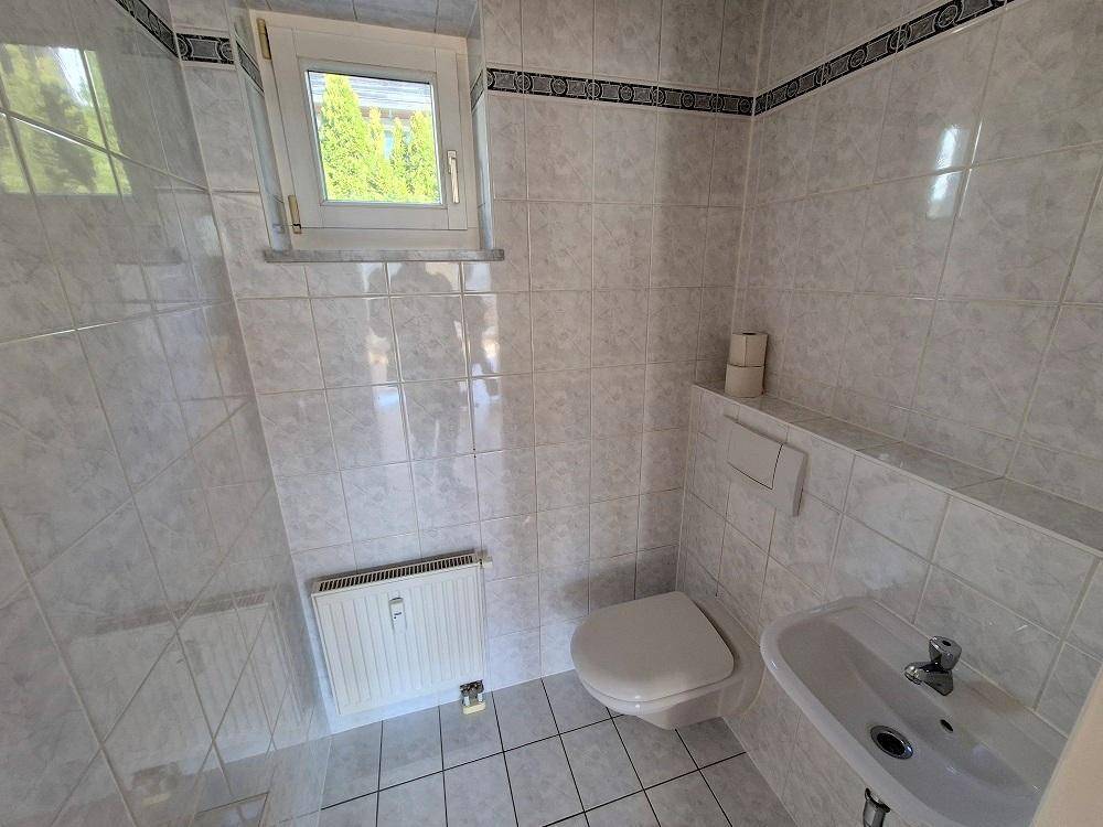 Separate Gästetoilette mit Fenster, WC und kleinem Handwaschbecken, hell gefliest.