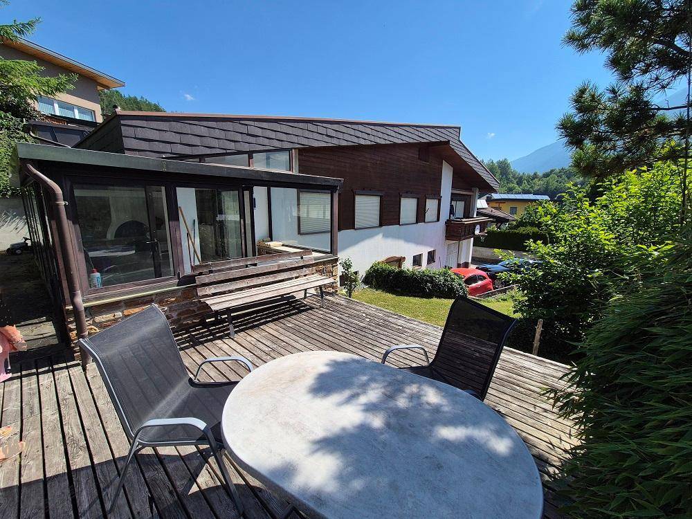 Holzterrasse mit Gartenmöbeln und Blick auf das Haus und die umliegende Berglandschaft.