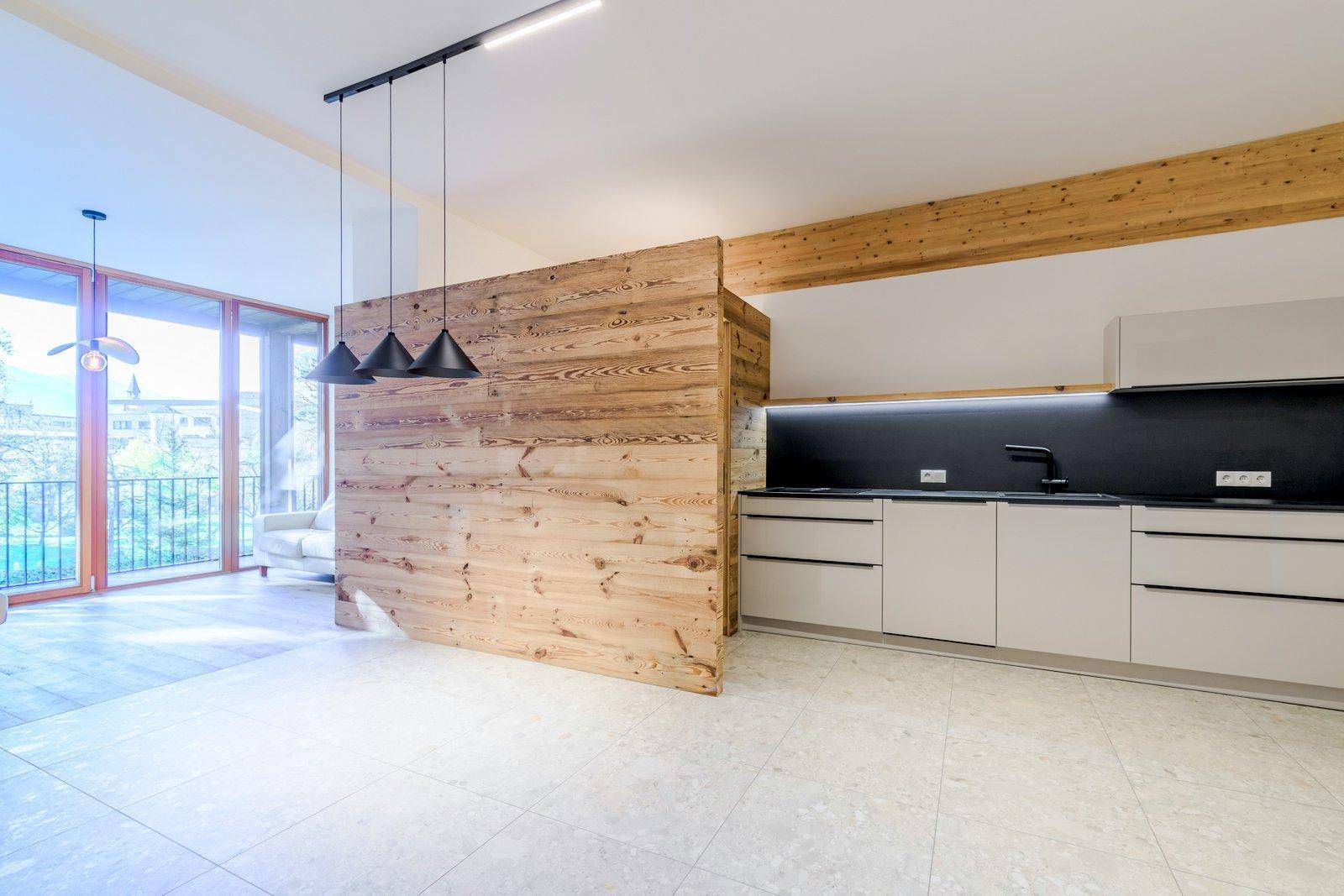 Offener Wohnbereich mit moderner Küche, Holzelementen und Zugang zu einem Balkon mit viel Tageslicht.